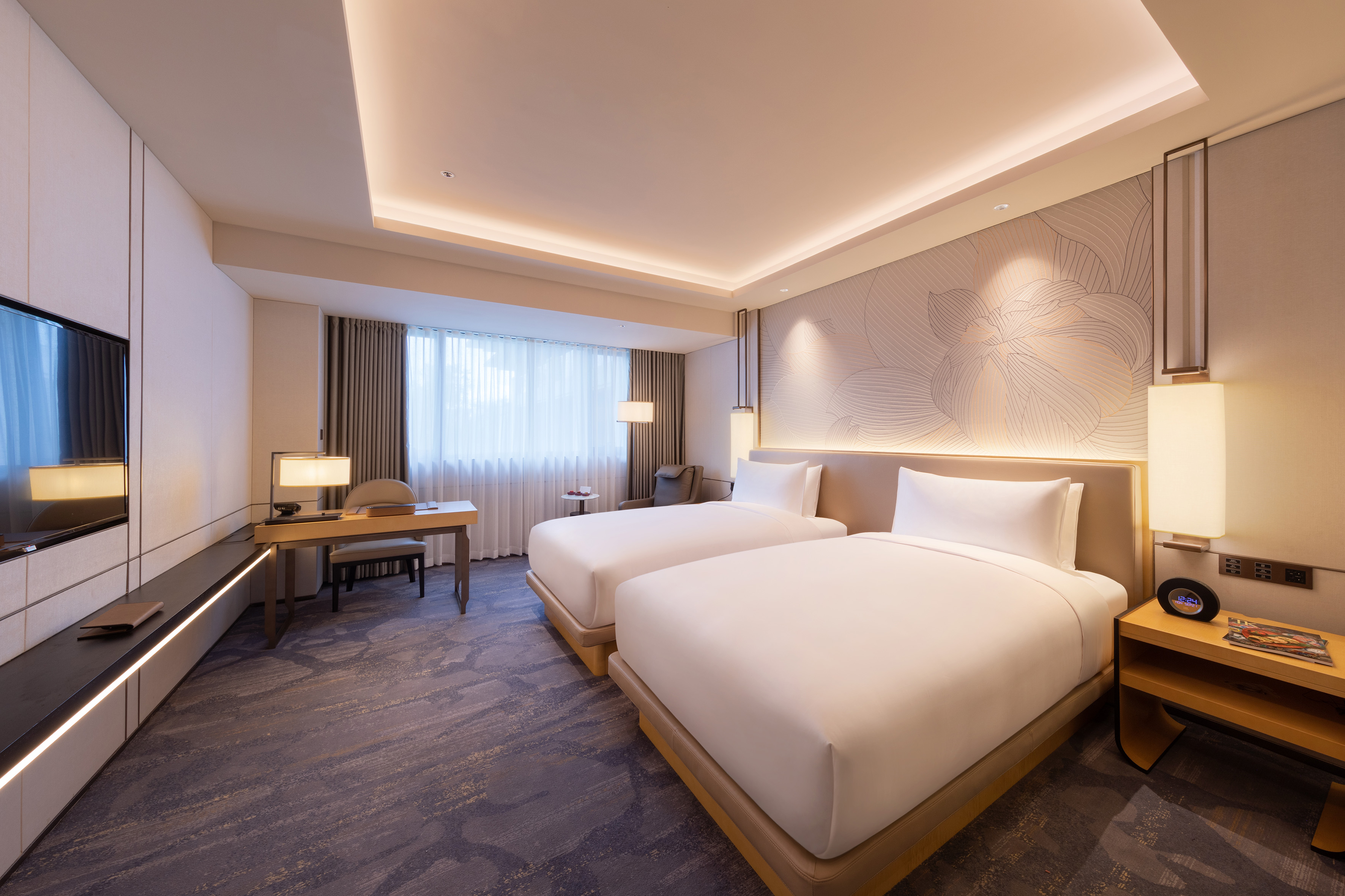 Modern hotel room with two twin beds, desk, flat-screen TV, and large window.