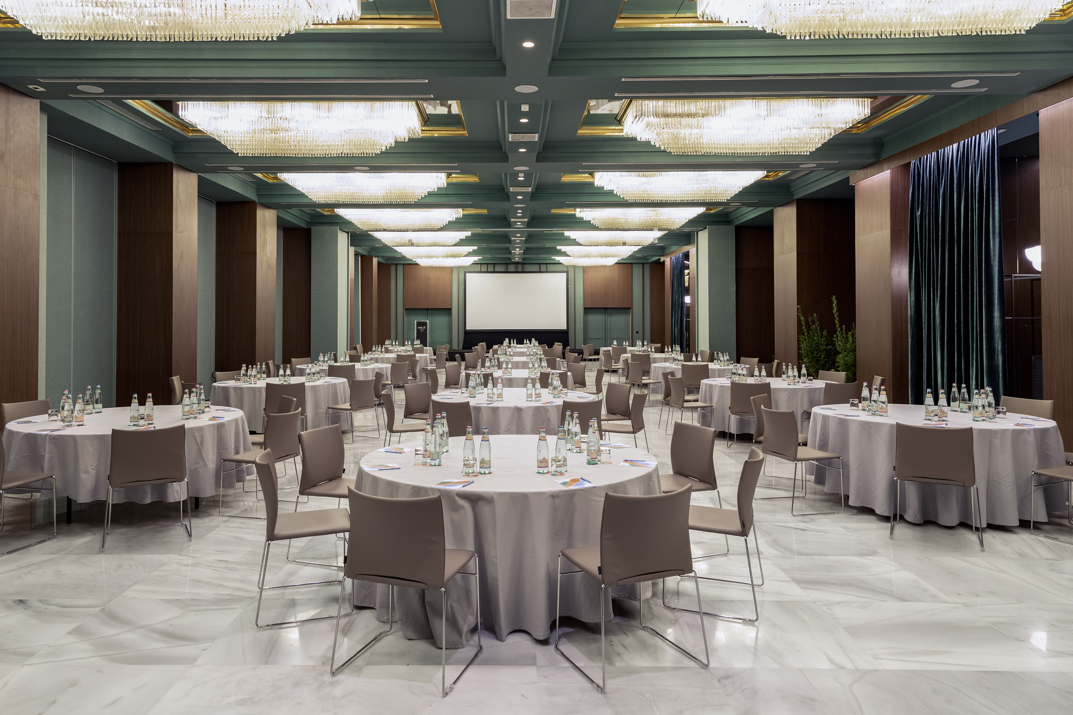 Large conference room with round tables, projection screen, and chandeliers.