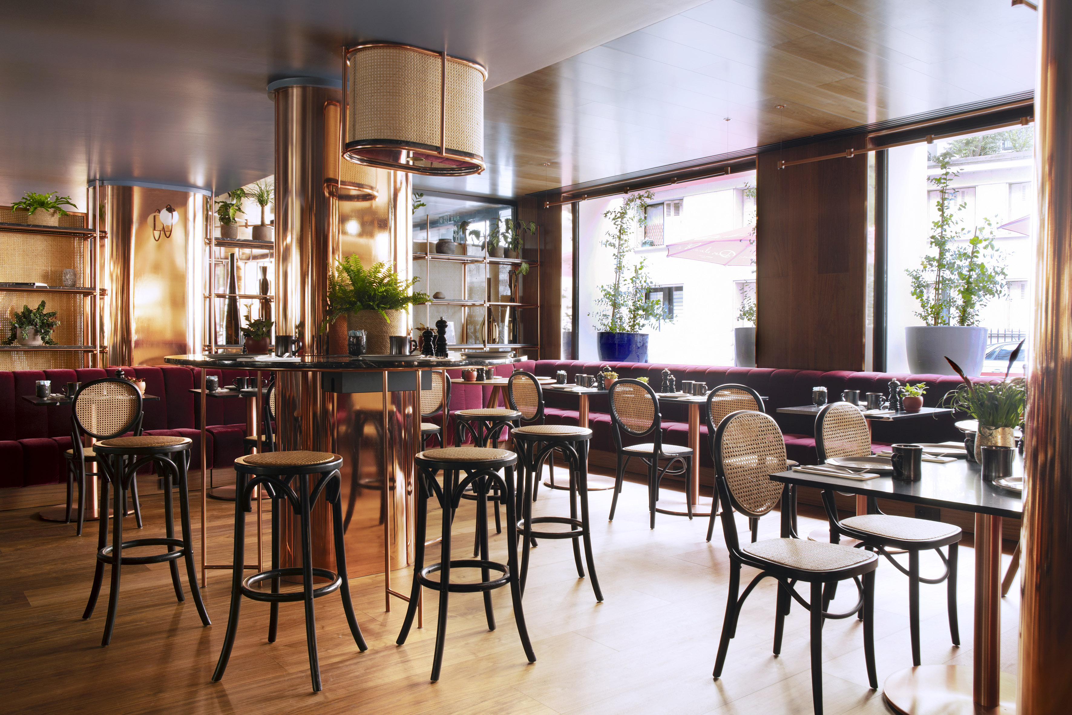 Chic restaurant interior with copper accents, rattan chairs, and red banquettes.