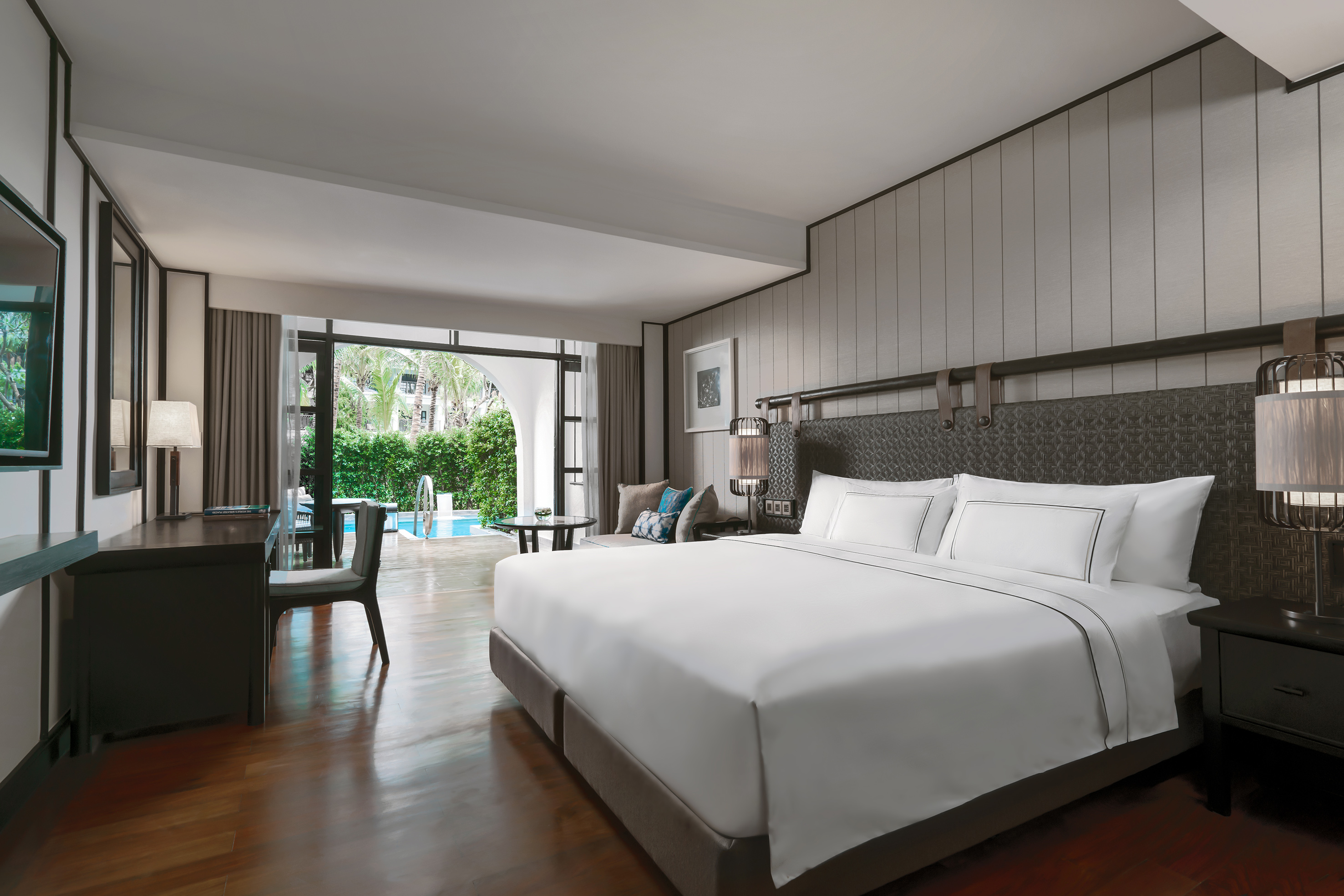 Luxury hotel suite with king bed, desk, and direct pool access from patio.