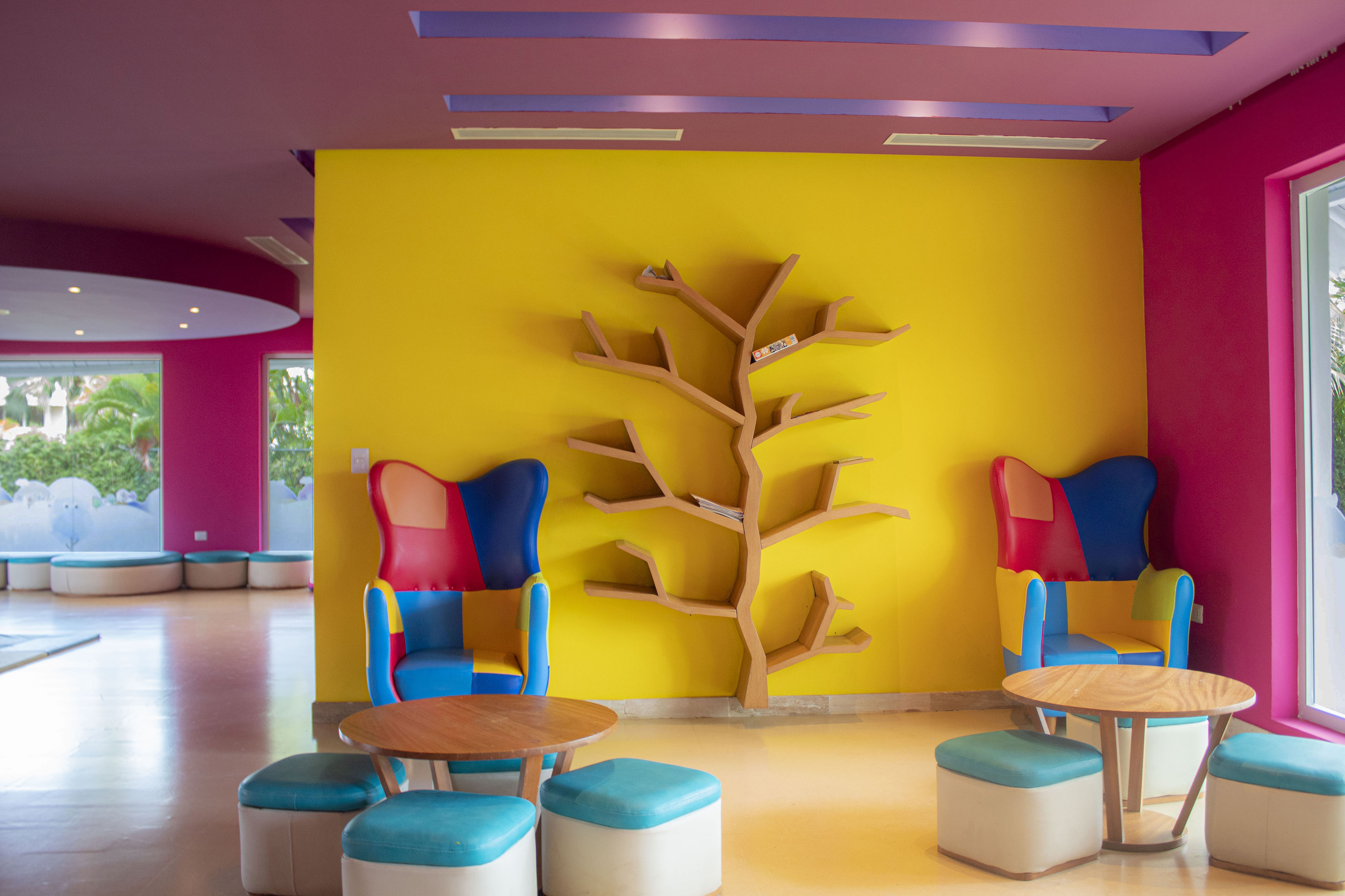 Vibrant children's play area with tree bookshelf, colorful furniture, yellow walls.
