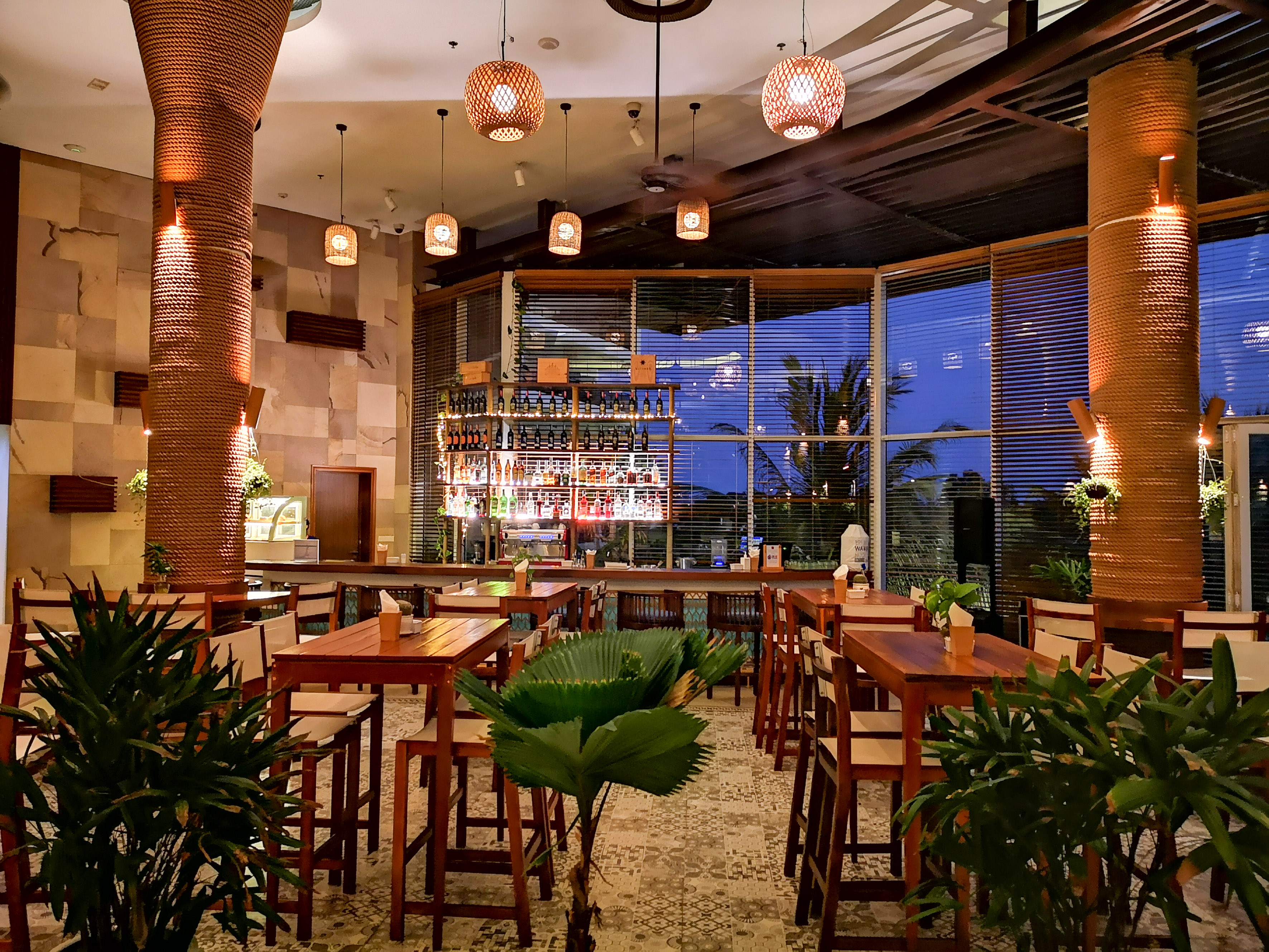Tropical restaurant bar with wooden tables, woven lights, and a stocked bar.