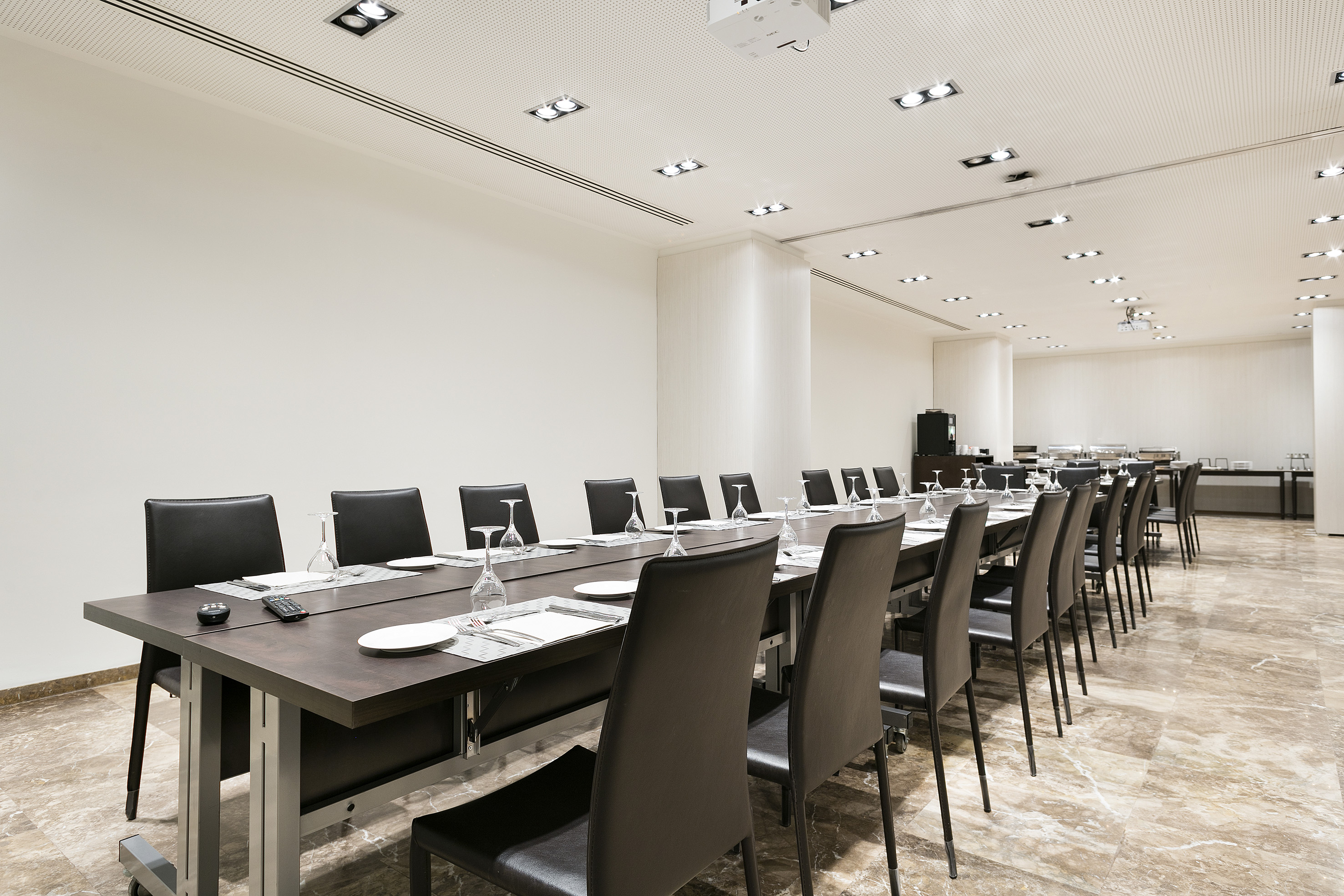 Modern conference room with long table, black chairs, projector, and buffet area.