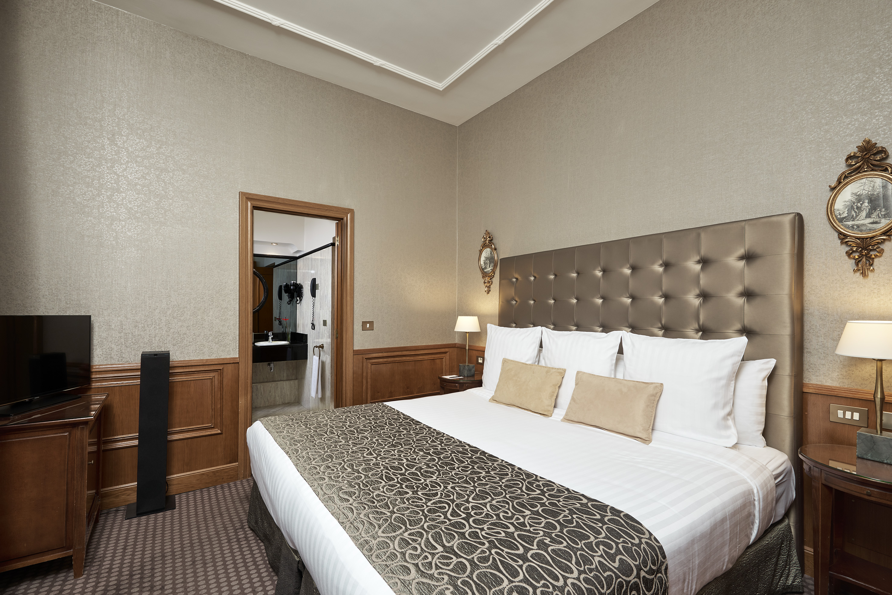 Elegant hotel bedroom with tufted bed, patterned runner, and ensuite bathroom.