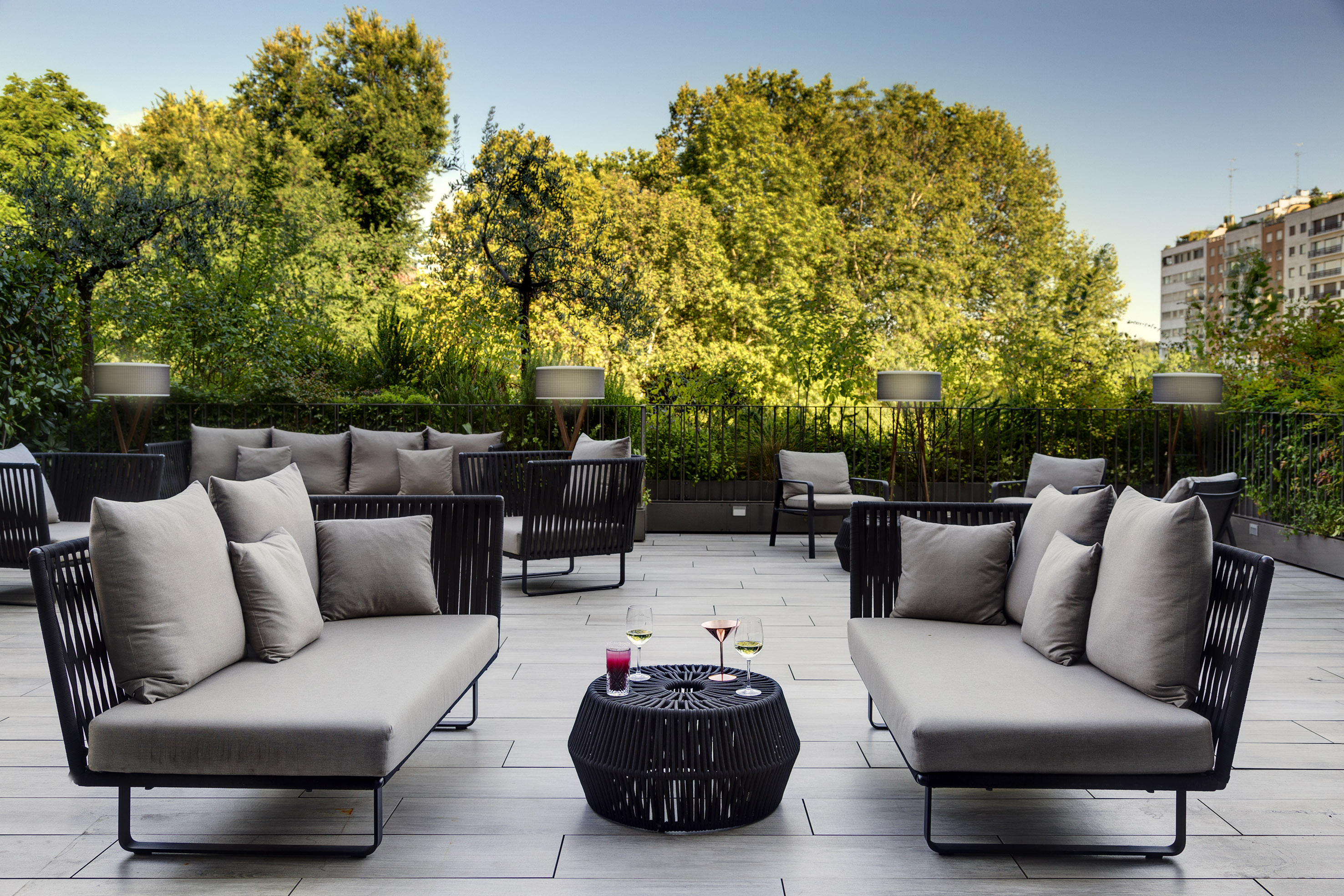 Modern outdoor lounge patio with drinks, gray sofas, and lush greenery.