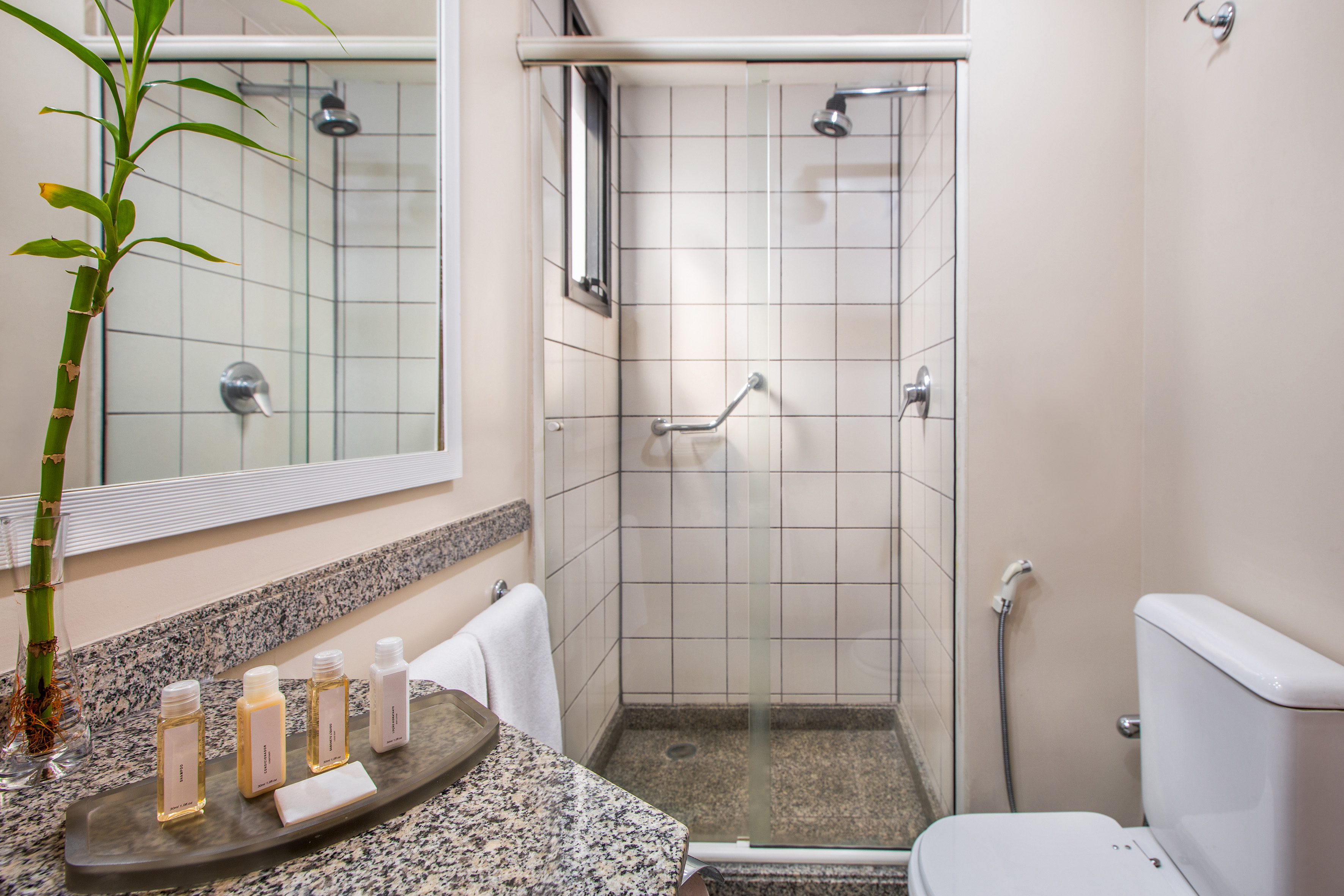 Modern hotel bathroom with shower, toilet, granite vanity, and toiletries.