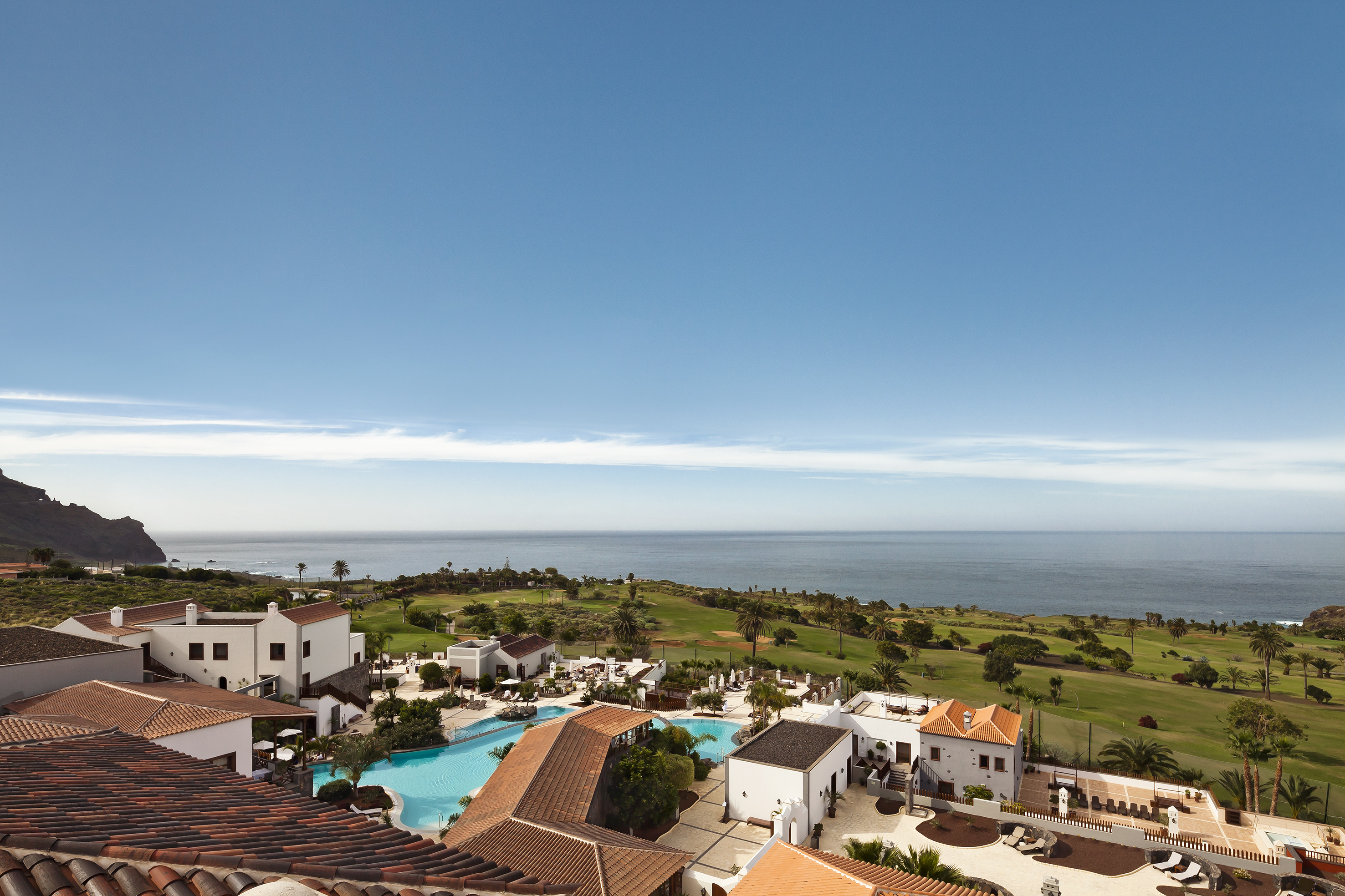 Oceanfront resort with pool, golf course, palm trees, and coastal cliff.