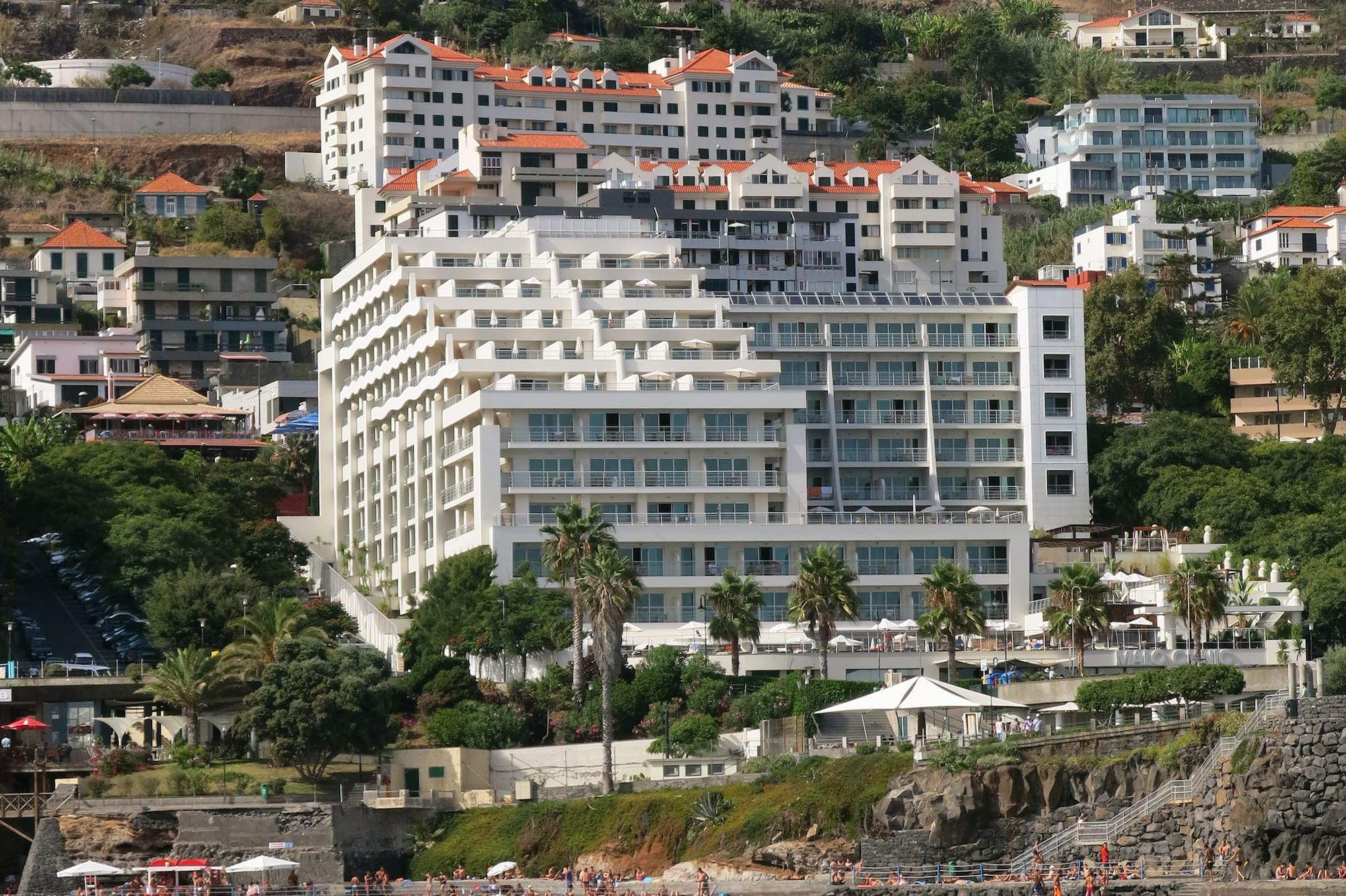 White hillside resort hotel on Madeira coast overlooking ocean and beach.