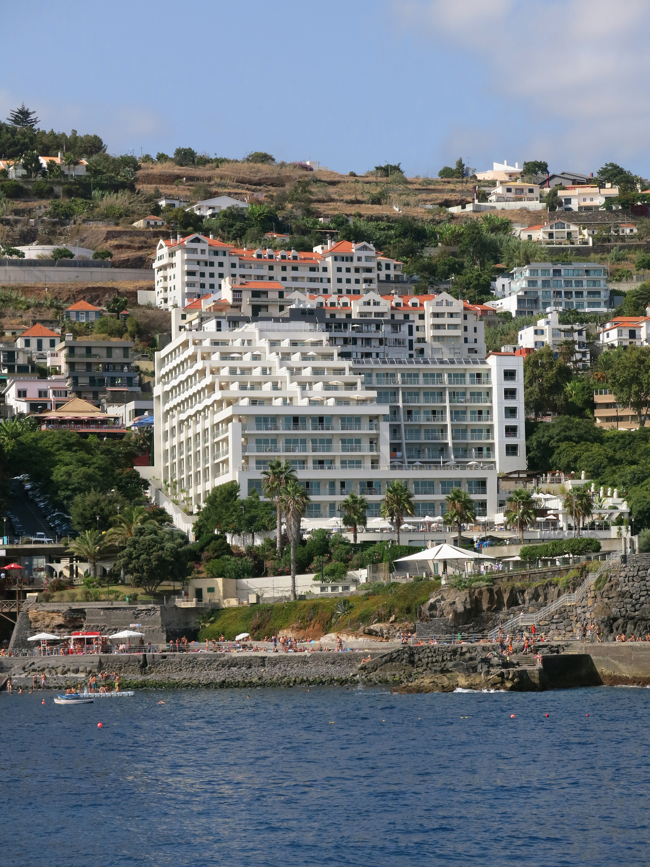 White hillside resort hotel on Madeira coast overlooking ocean and beach.