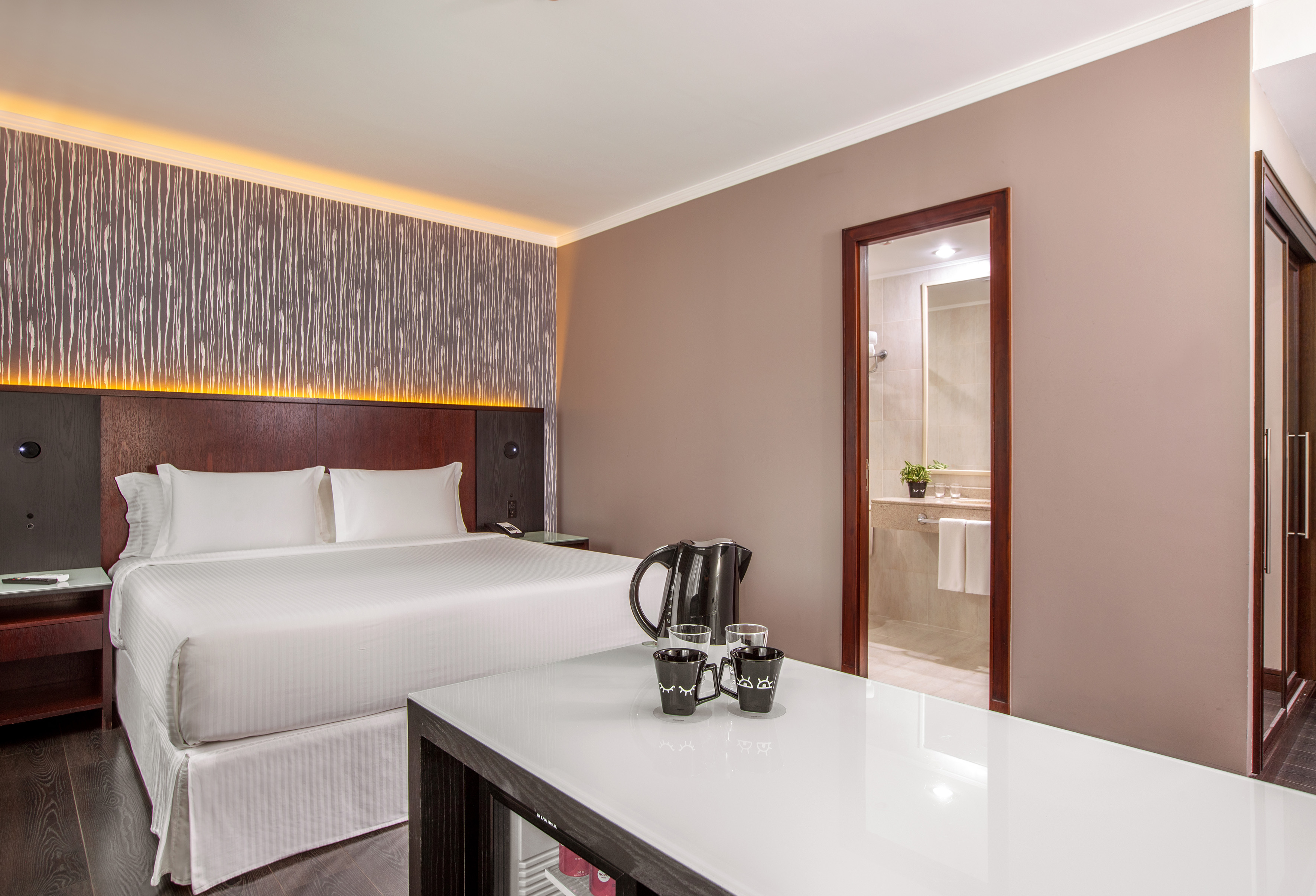 Modern hotel room with king bed, ambient lighting, and en-suite bathroom.