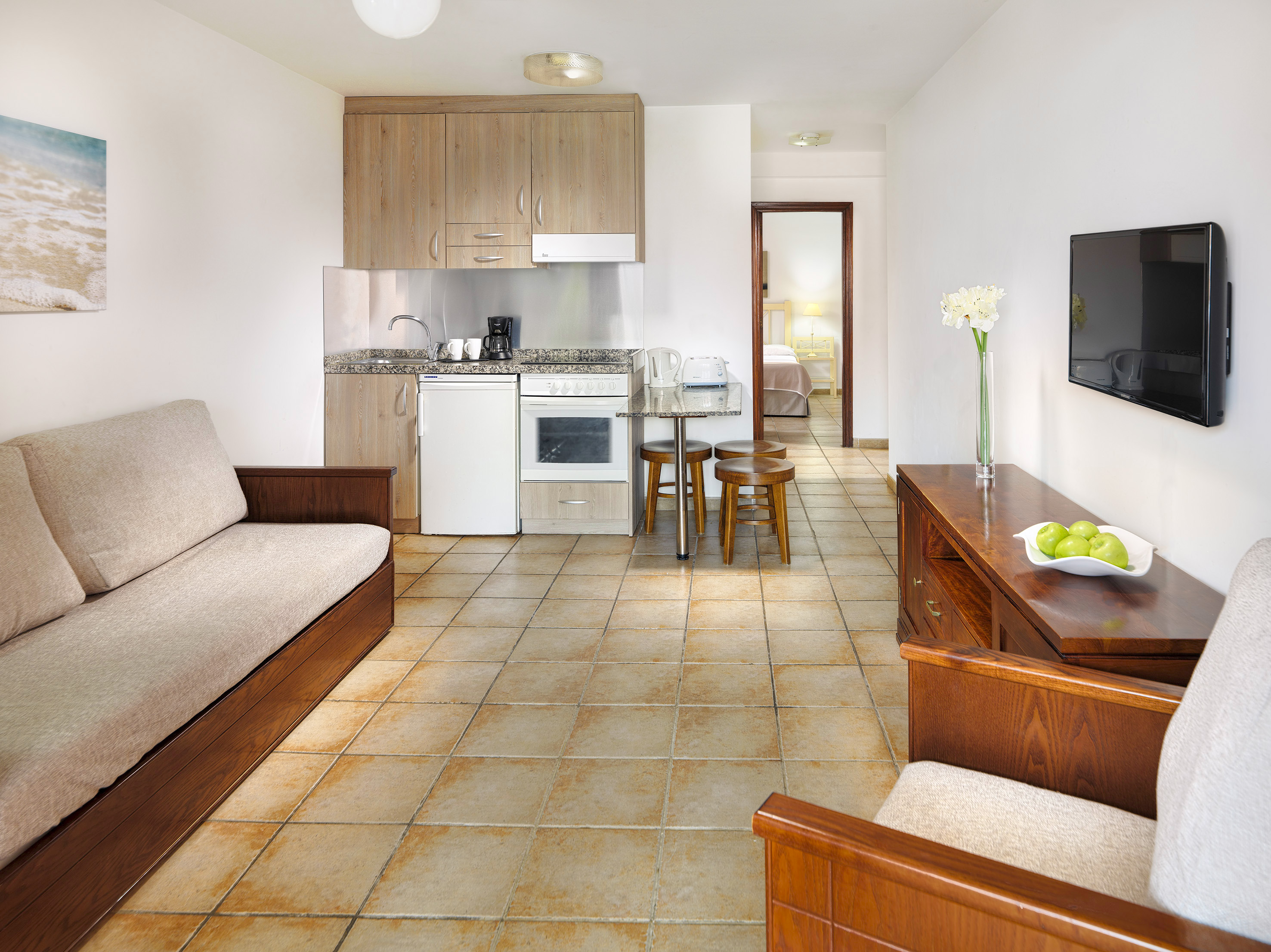 Modern studio apartment with kitchenette, living area, sofa, TV, and bedroom entrance.