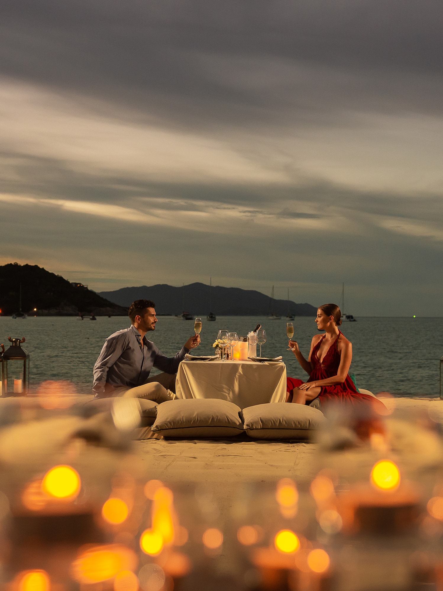 a man and woman sitting at a table with wine glasses on the beach
