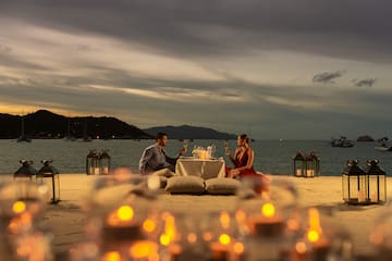 a man and woman sitting at a table with wine glasses on the beach