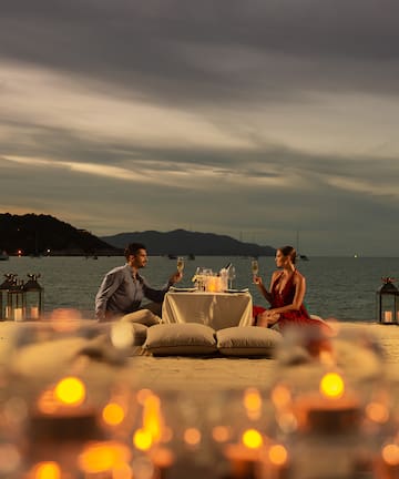 a man and woman sitting at a table with wine glasses on the beach