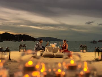 a man and woman sitting at a table with wine glasses on the beach
