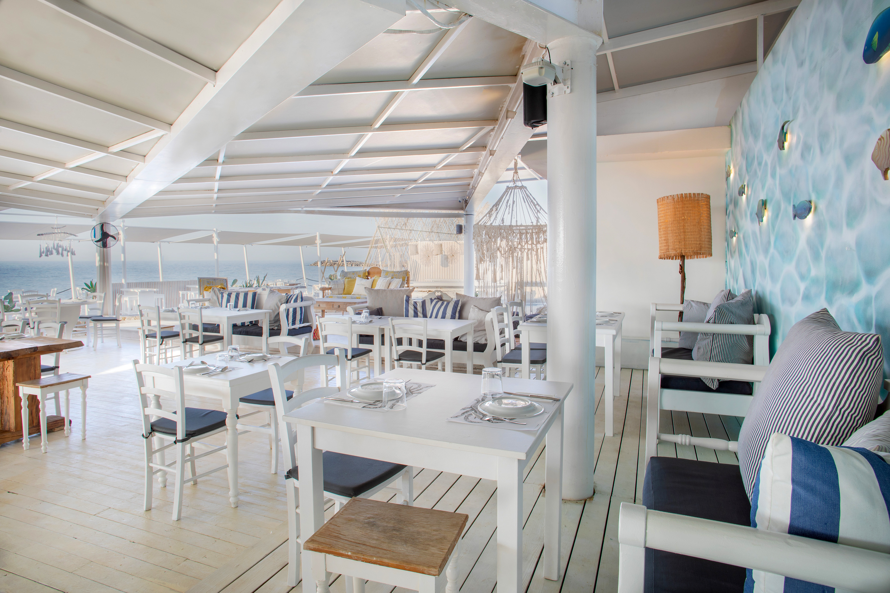 Coastal restaurant with white furniture, blue striped cushions, and ocean view.