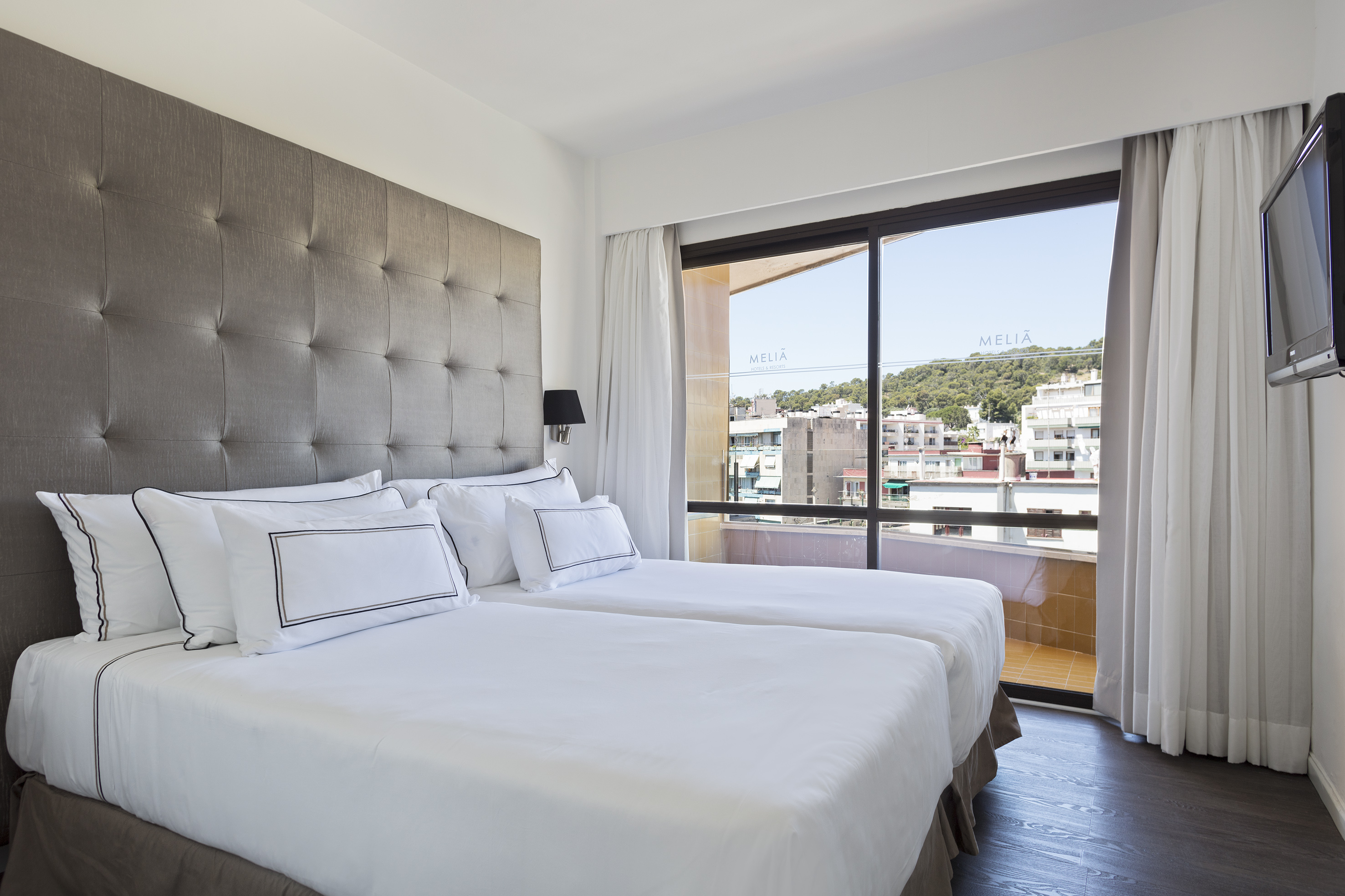 Melia hotel room with twin beds, gray headboard, and city view balcony.