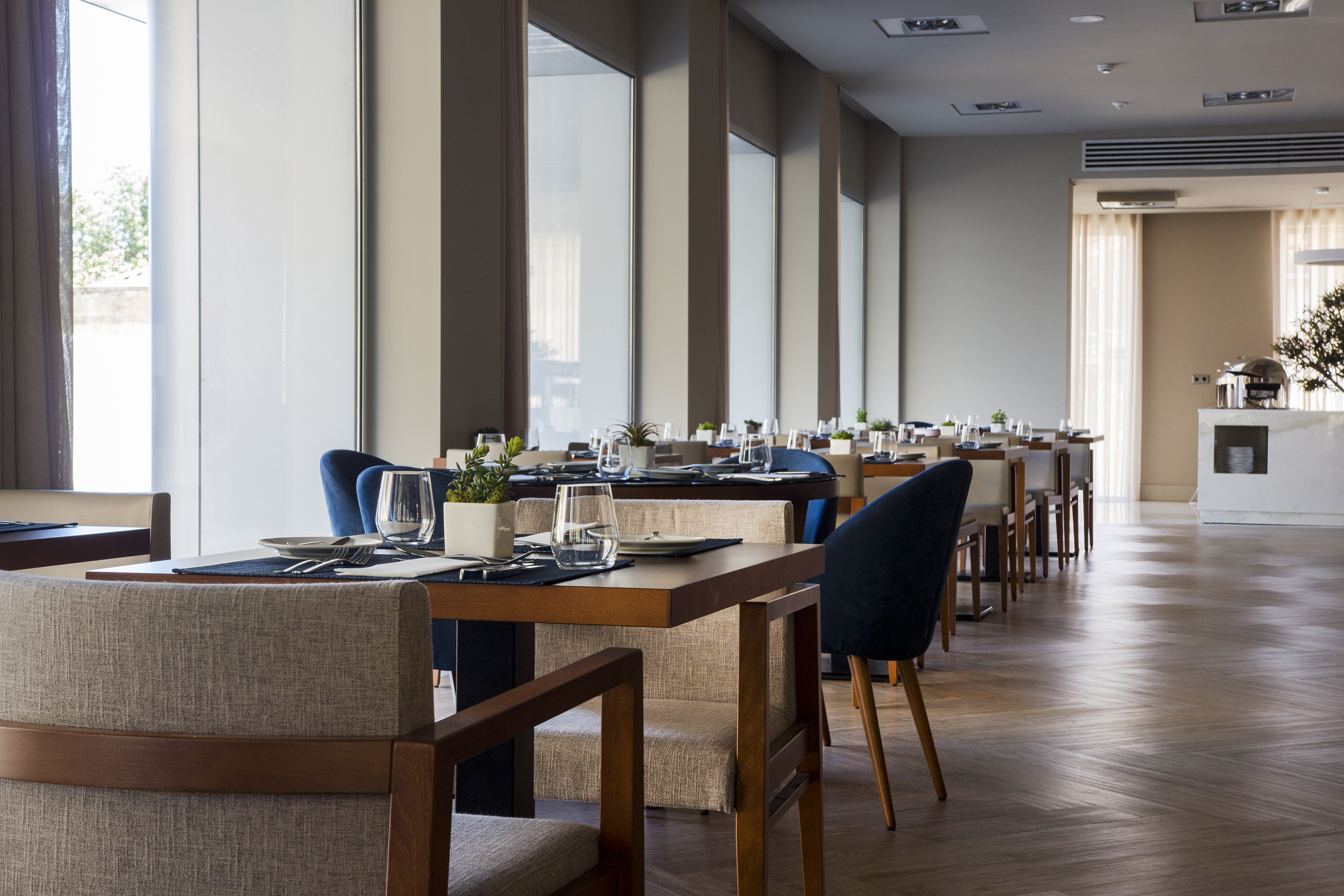 Modern restaurant dining area with set tables, blue chairs, and large windows.