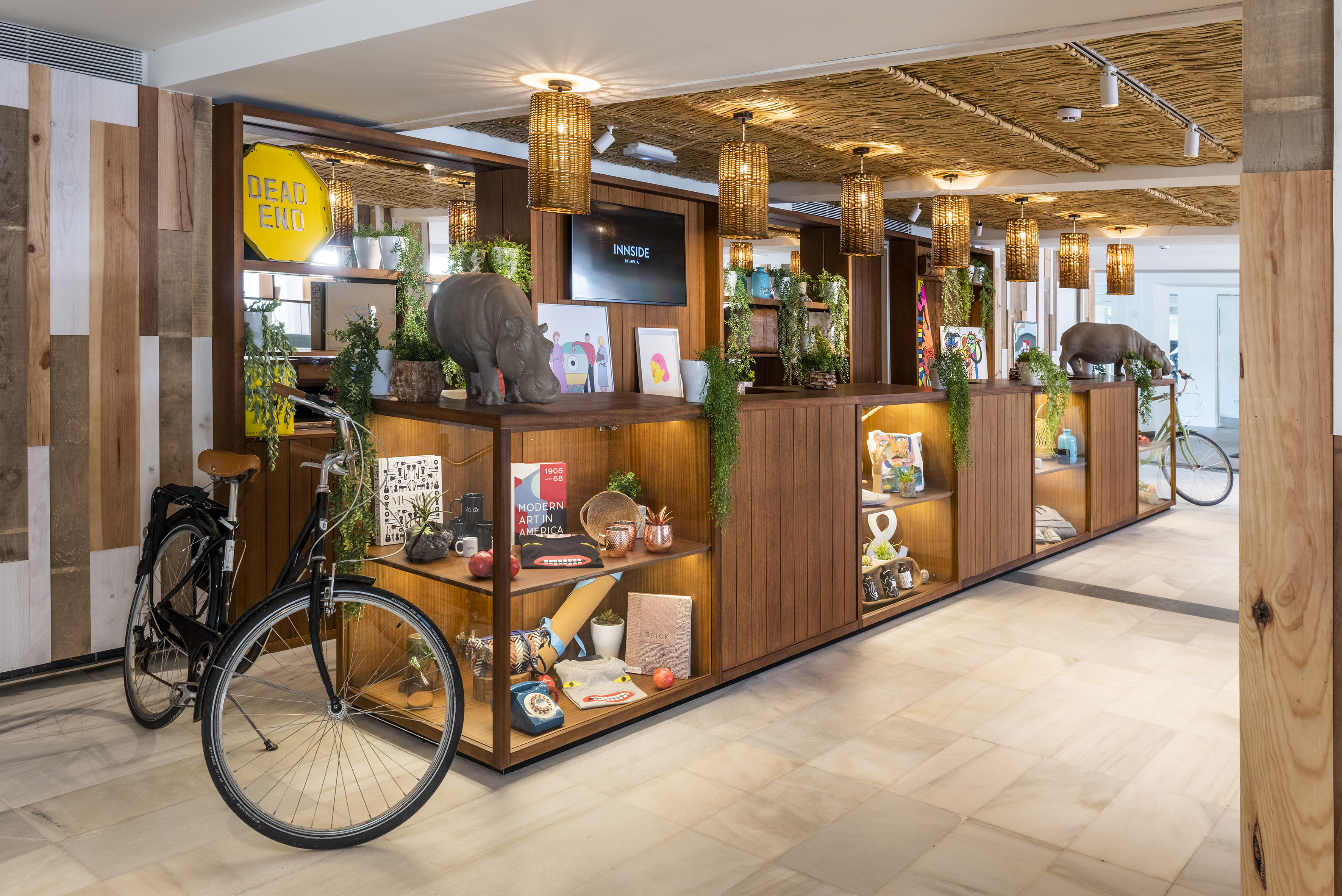 Modern hotel lobby featuring decorative wooden shelving, rhino, bikes, and plants.