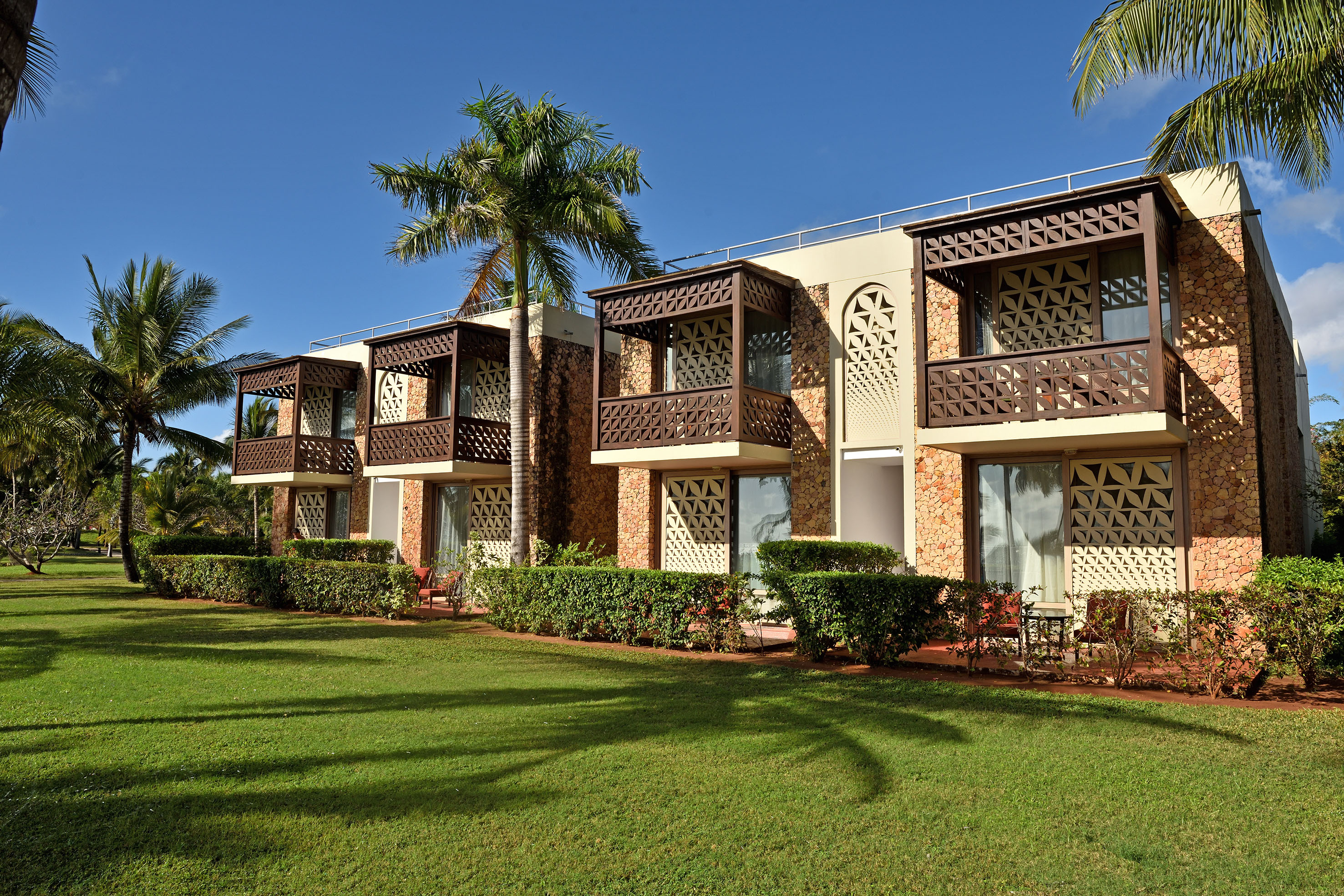 Tropical resort building with stone facade, ornate wooden balconies, palm trees.