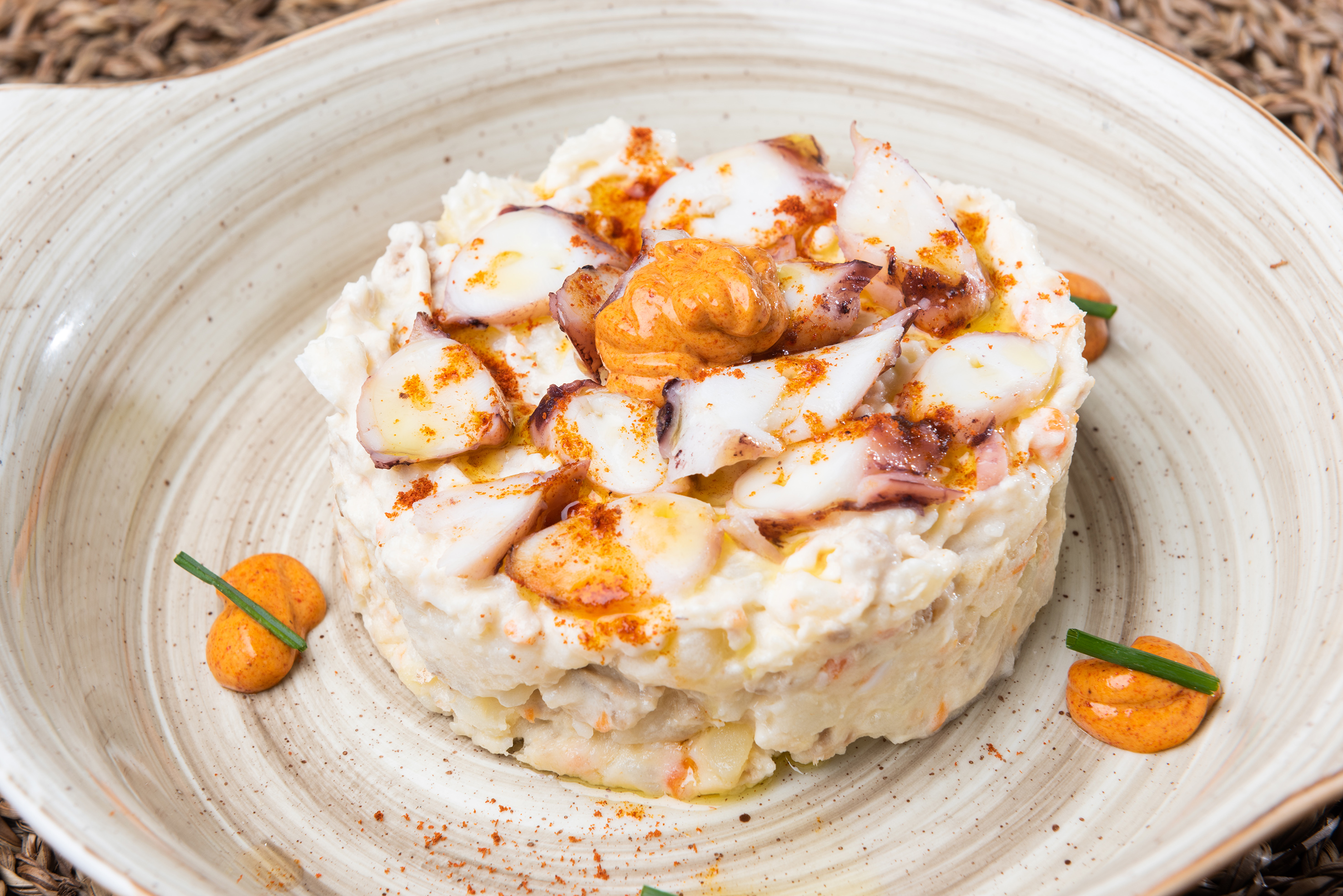 Creamy potato salad topped with sliced octopus, paprika, and chives on a plate.