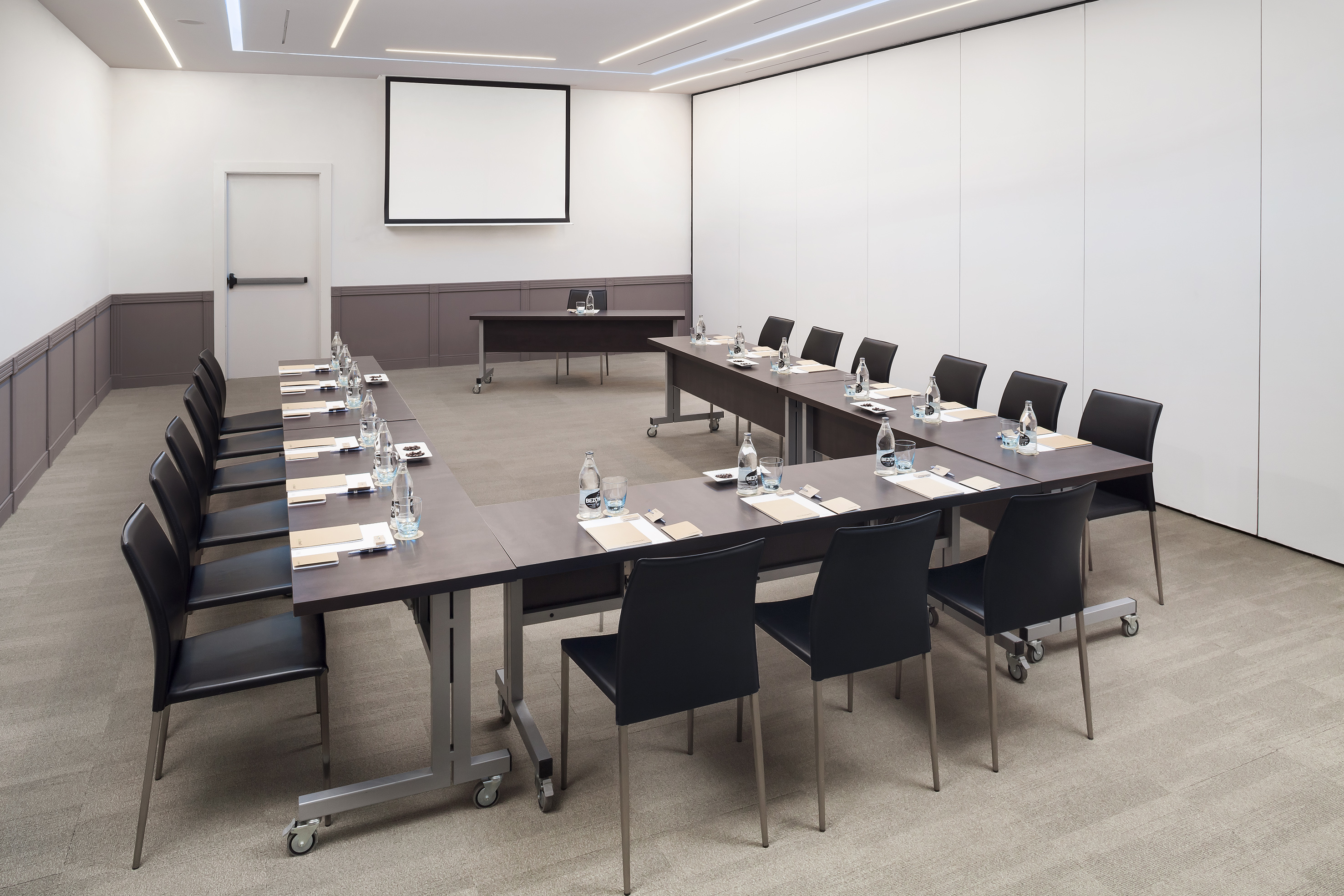 U-shaped meeting room setup with projector screen, modern tables and chairs.