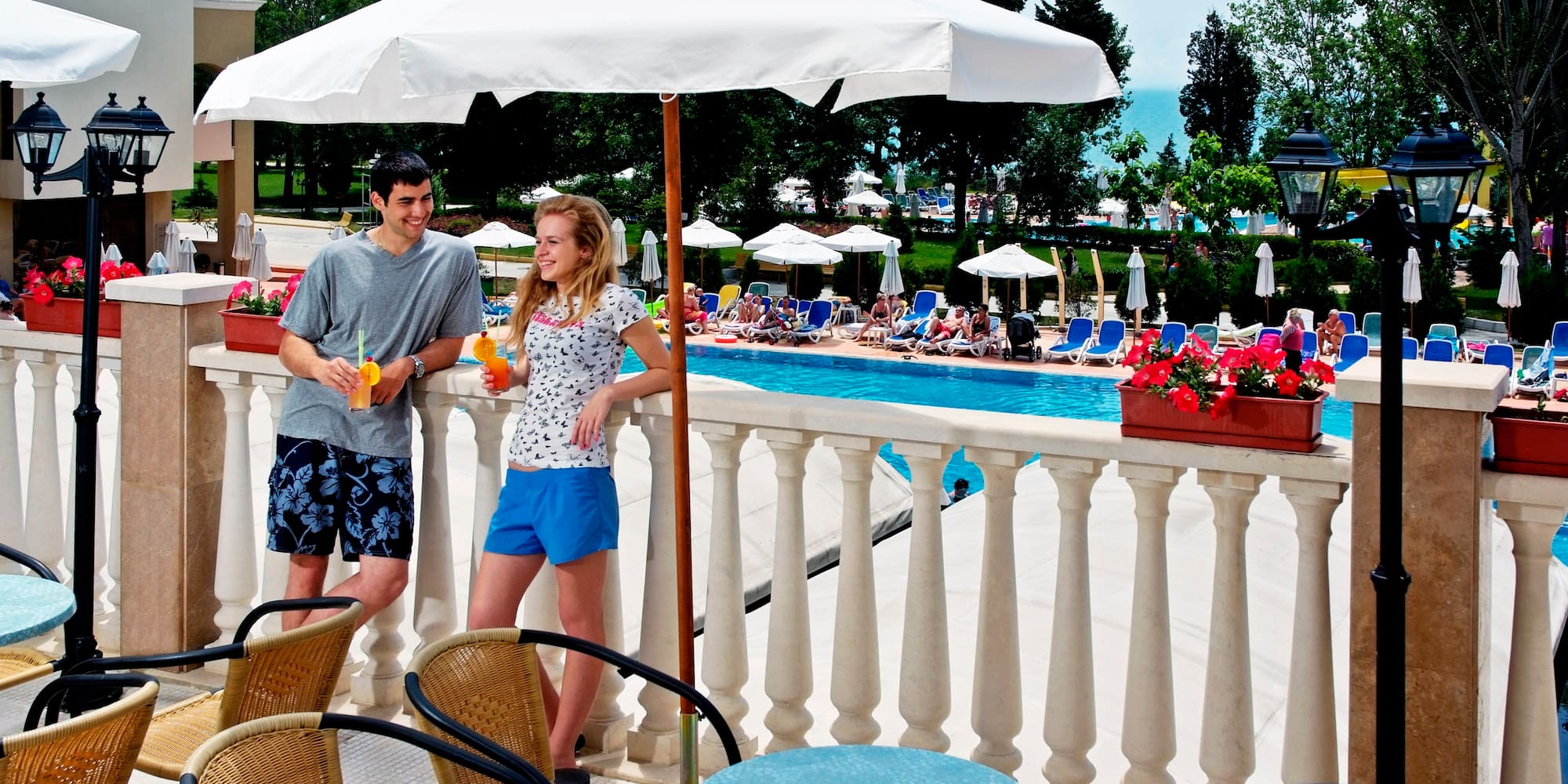 a man and woman standing on a balcony with umbrellas and chairs