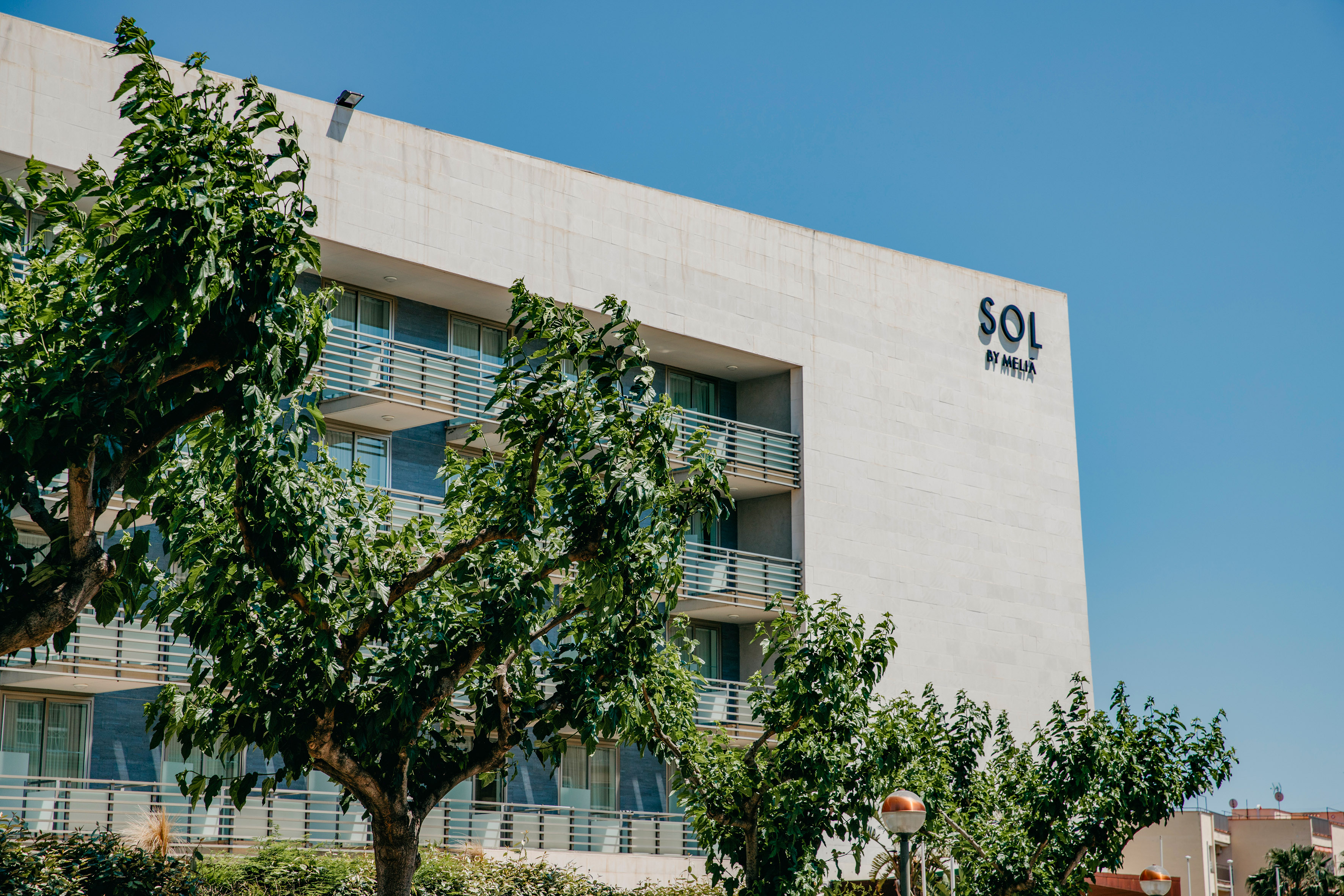 Sol by Melia hotel exterior, white facade, balconies, and green trees.