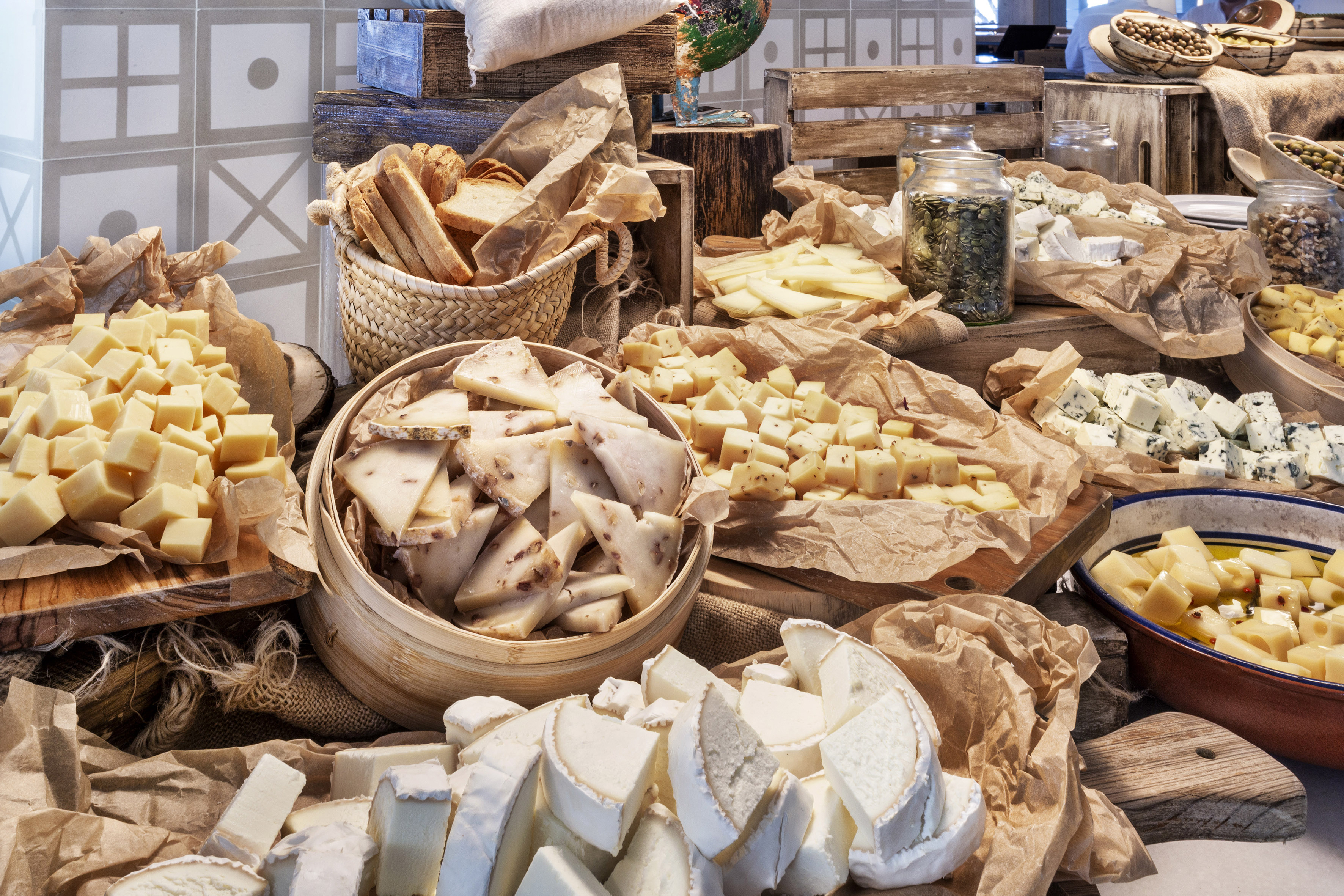 Gourmet cheese buffet featuring various types, bread, and olives on display.