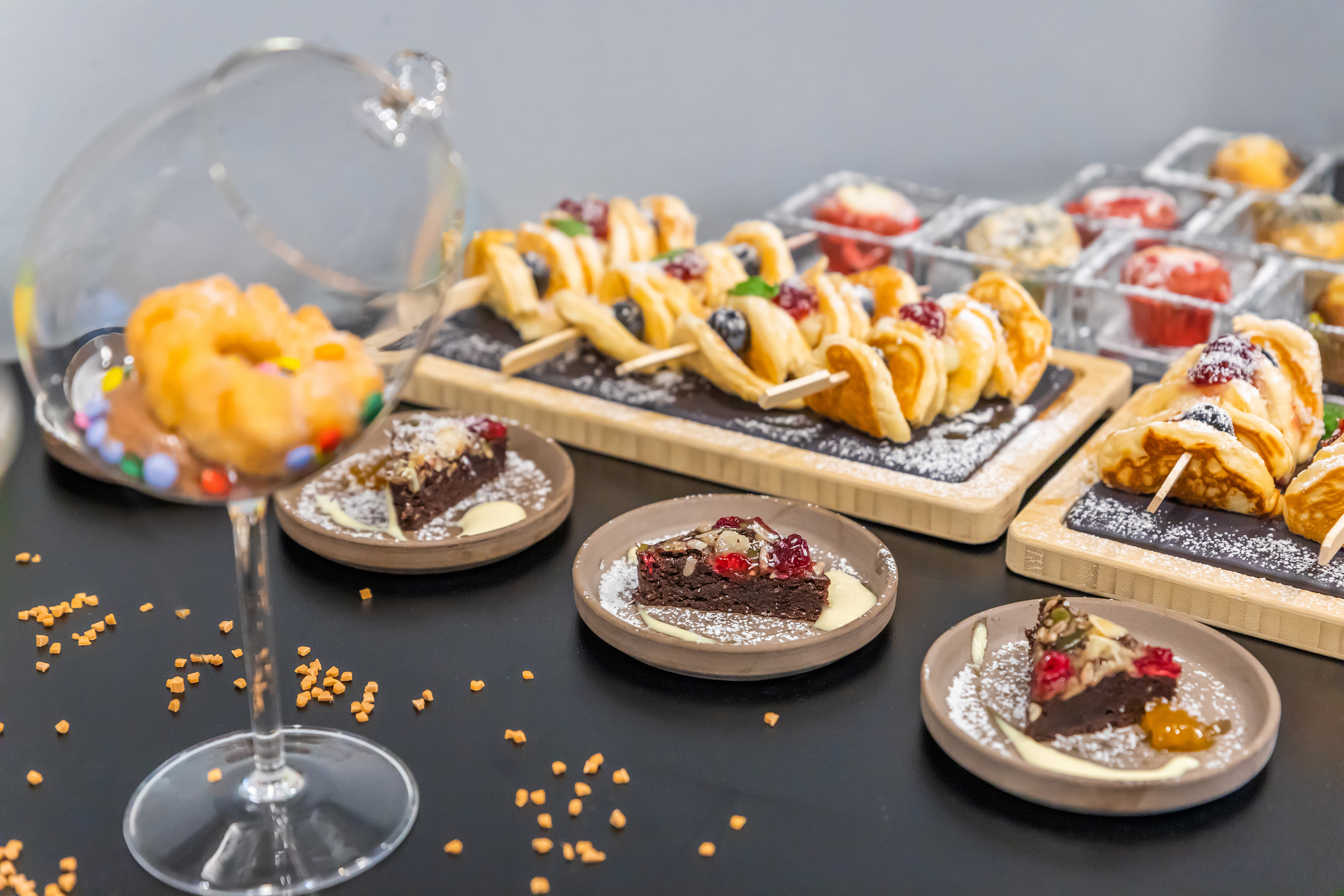 Dessert bar with mini pancake skewers, brownie slices, and donut in glass.
