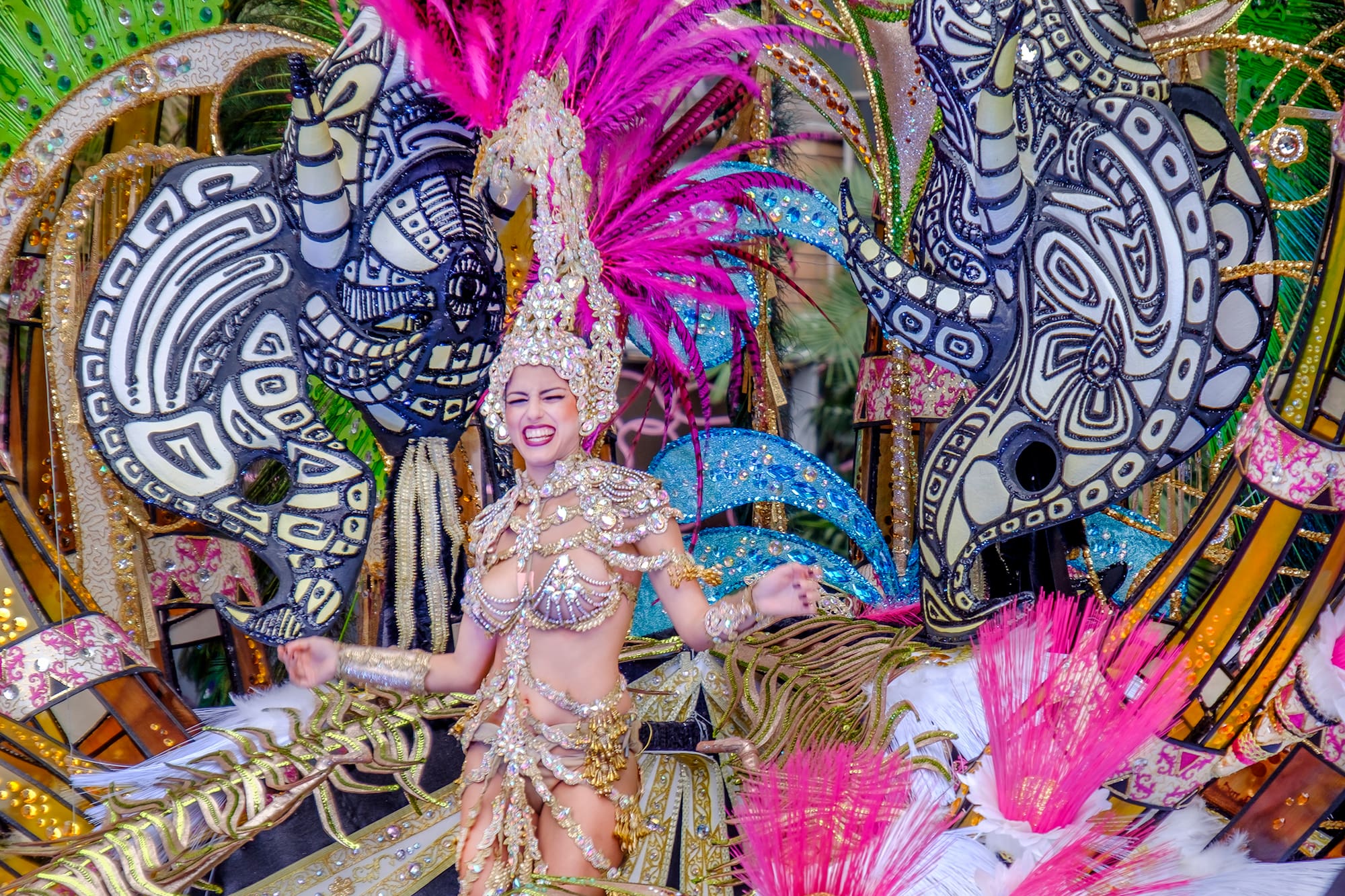 Reina de carnaval con vestido de oro y plumas fucsia, desfile festivo.