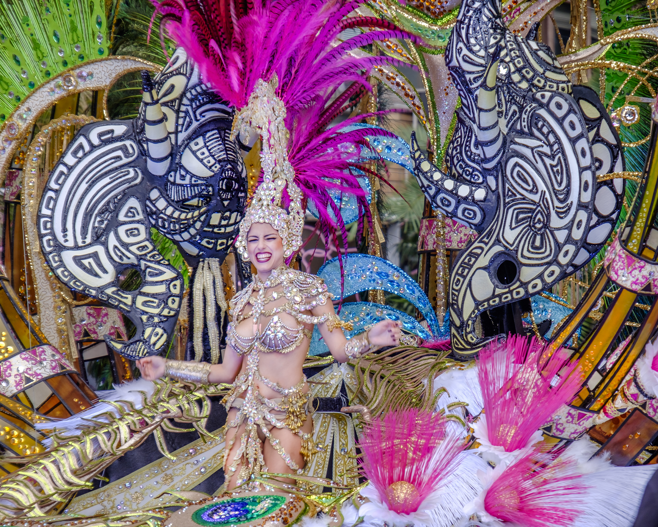 Reina de carnaval con vestido de oro y plumas fucsia, desfile festivo.