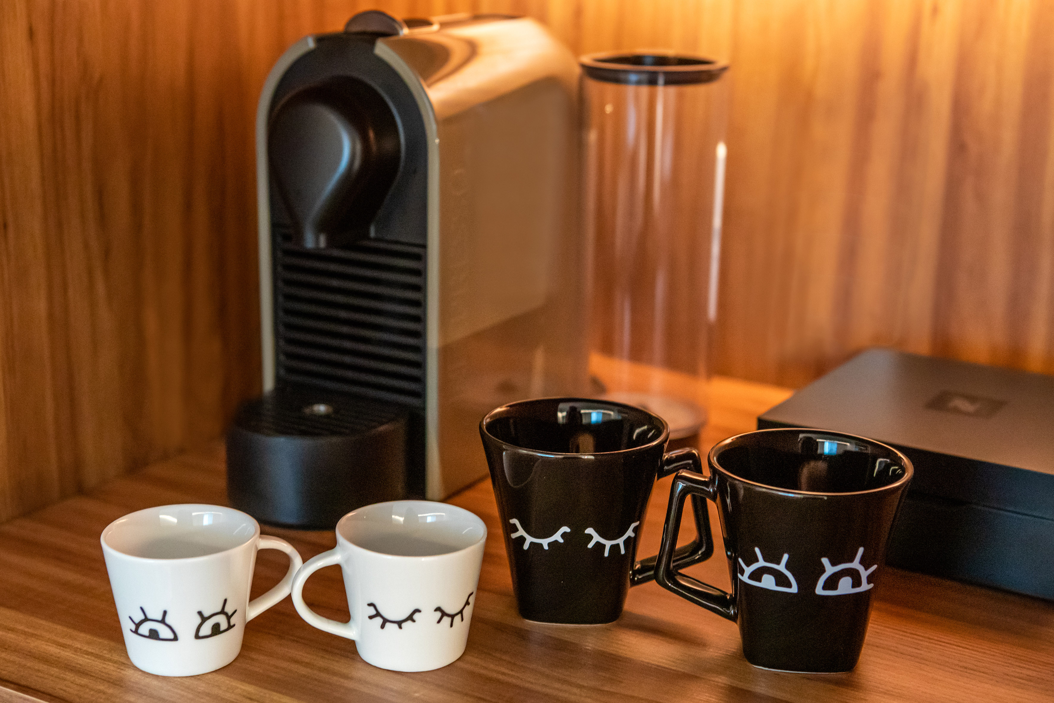 Nespresso machine with four eye-design coffee mugs on a wooden counter.