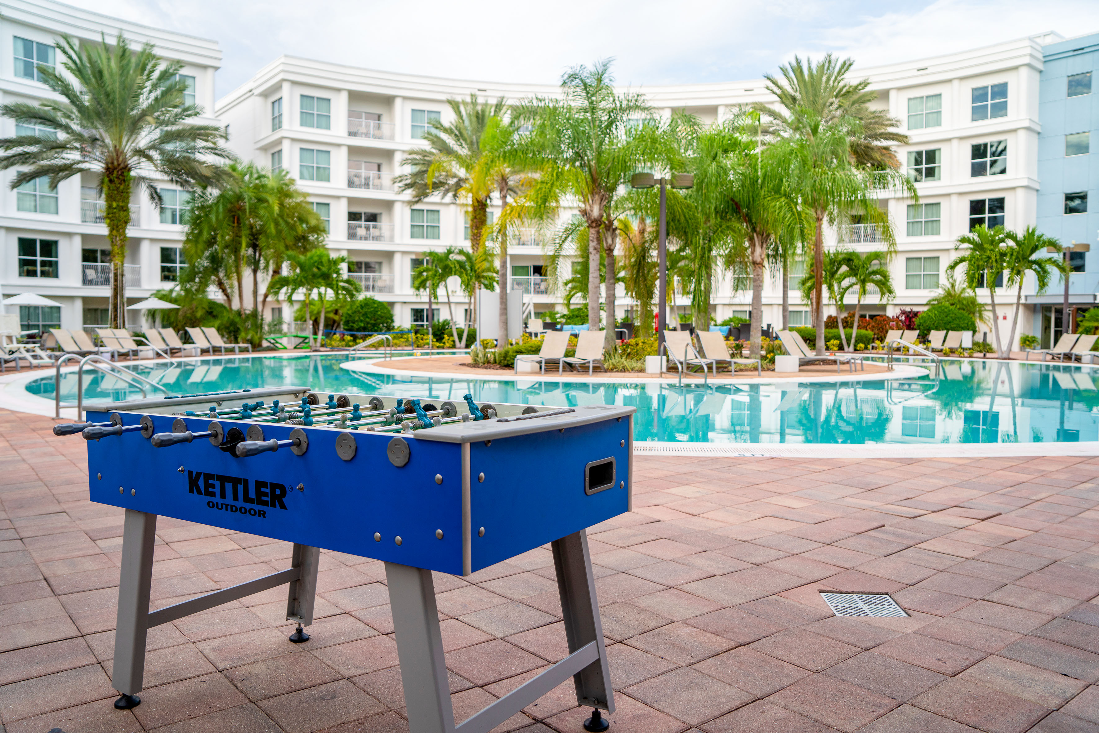 Blue Kettler outdoor foosball table by a hotel pool with palm trees.