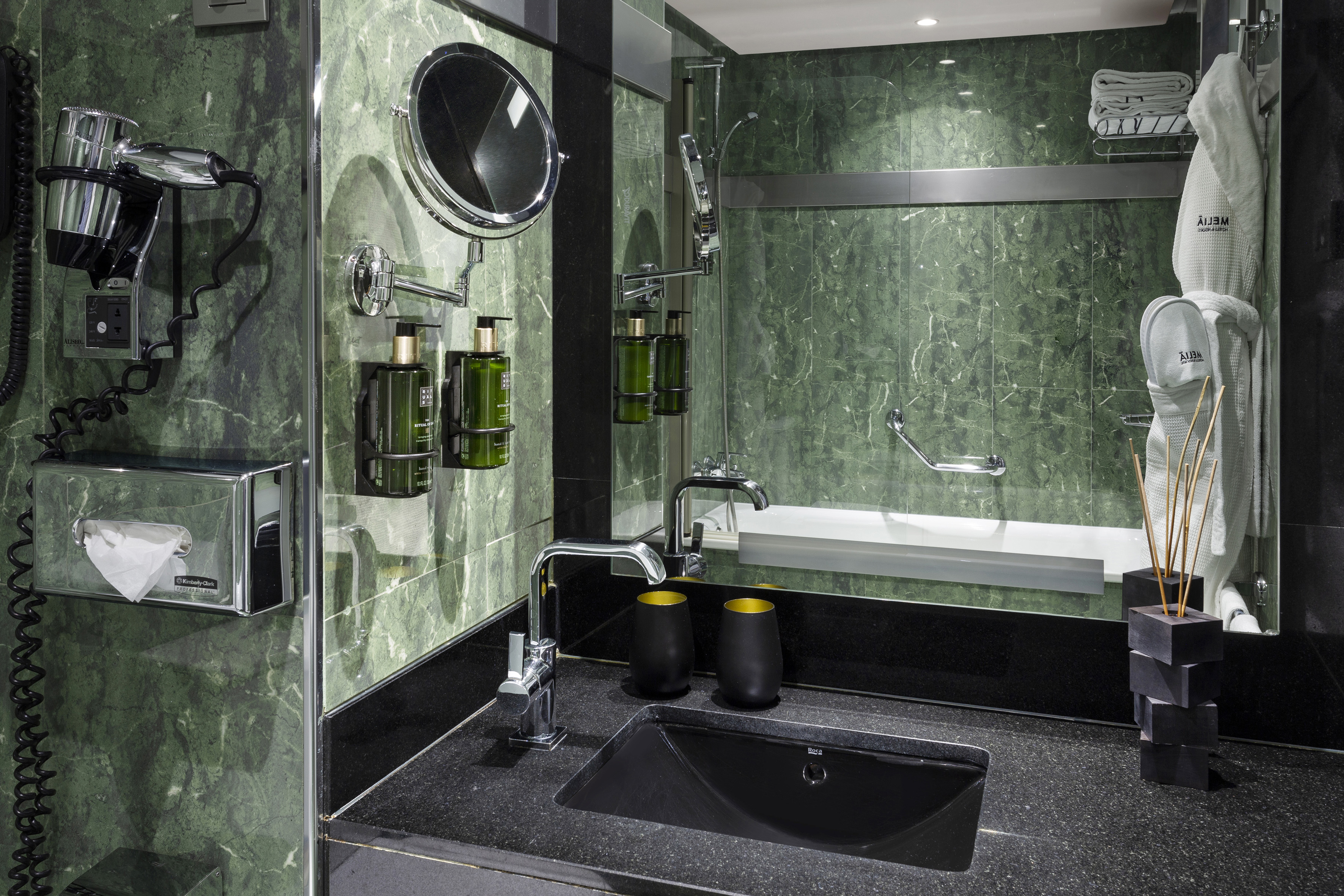 Green marble bathroom with black sink, chrome fixtures, and bath amenities.