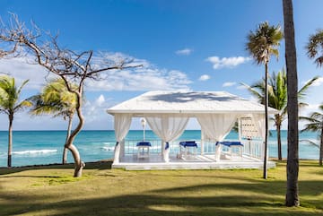 a white gazebo with blue and white curtains and a beach in the background