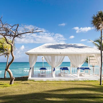 a white gazebo with blue and white curtains and a beach in the background