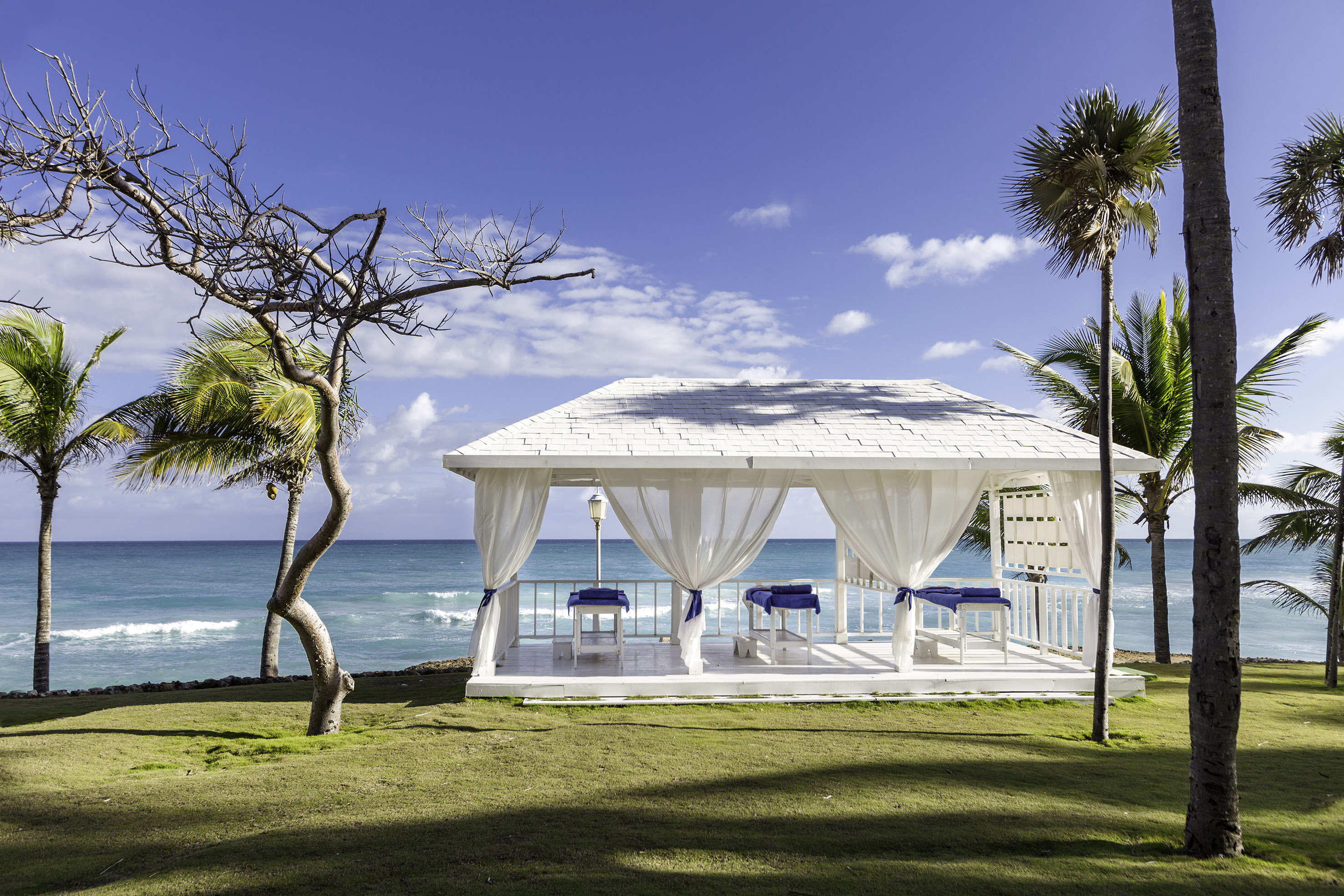 a white gazebo with blue and white curtains and a beach in the background