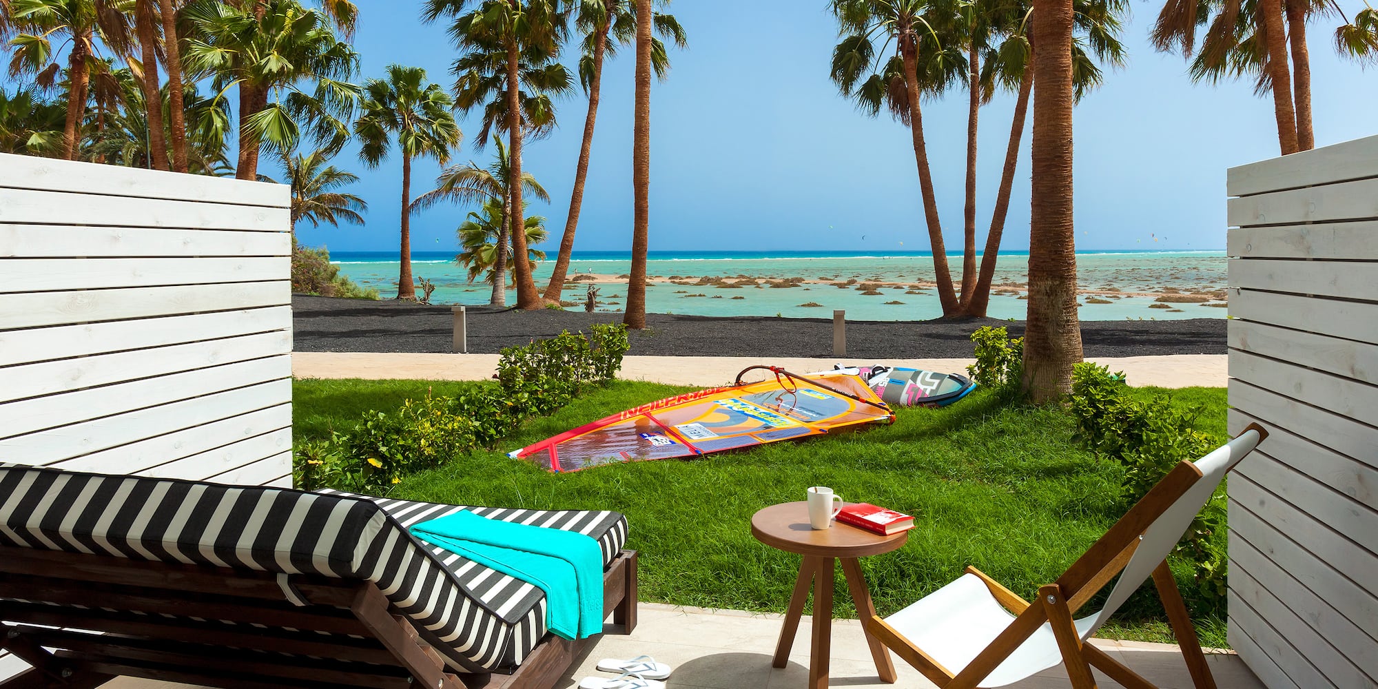 a deck chairs and a table on a patio with palm trees and a beach