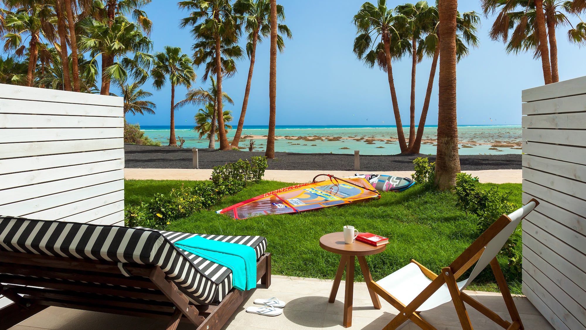 a deck chairs and a table on a patio with palm trees and a beach