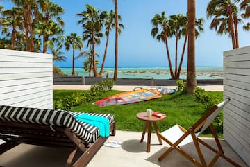 a deck chairs and a table on a patio with palm trees and a beach