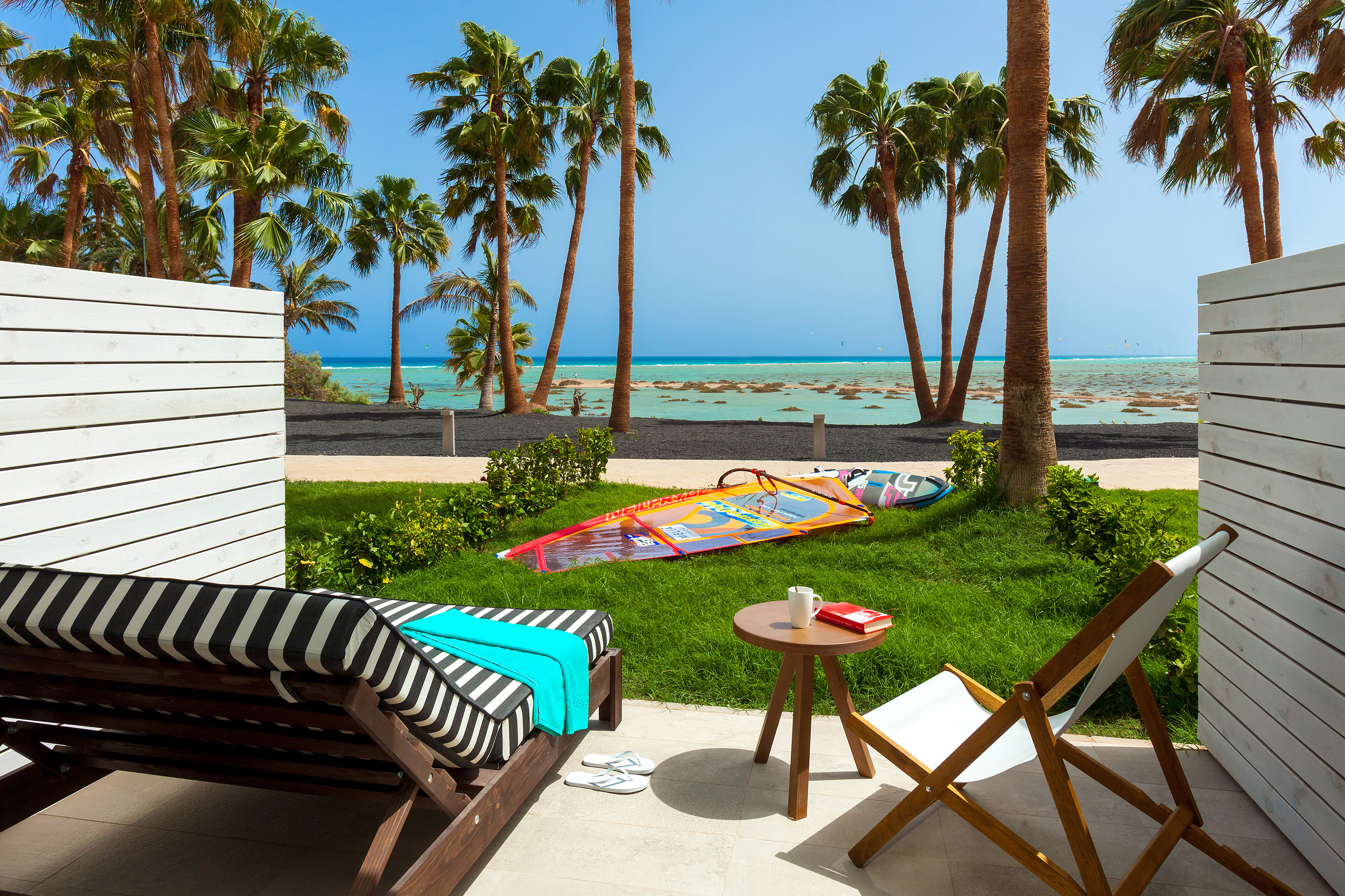 a deck chairs and a table on a patio with palm trees and a beach