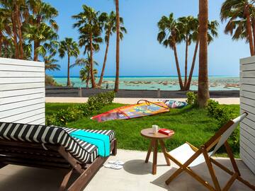 a deck chairs and a table on a patio with palm trees and a beach