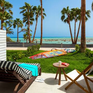 a deck chairs and a table on a patio with palm trees and a beach