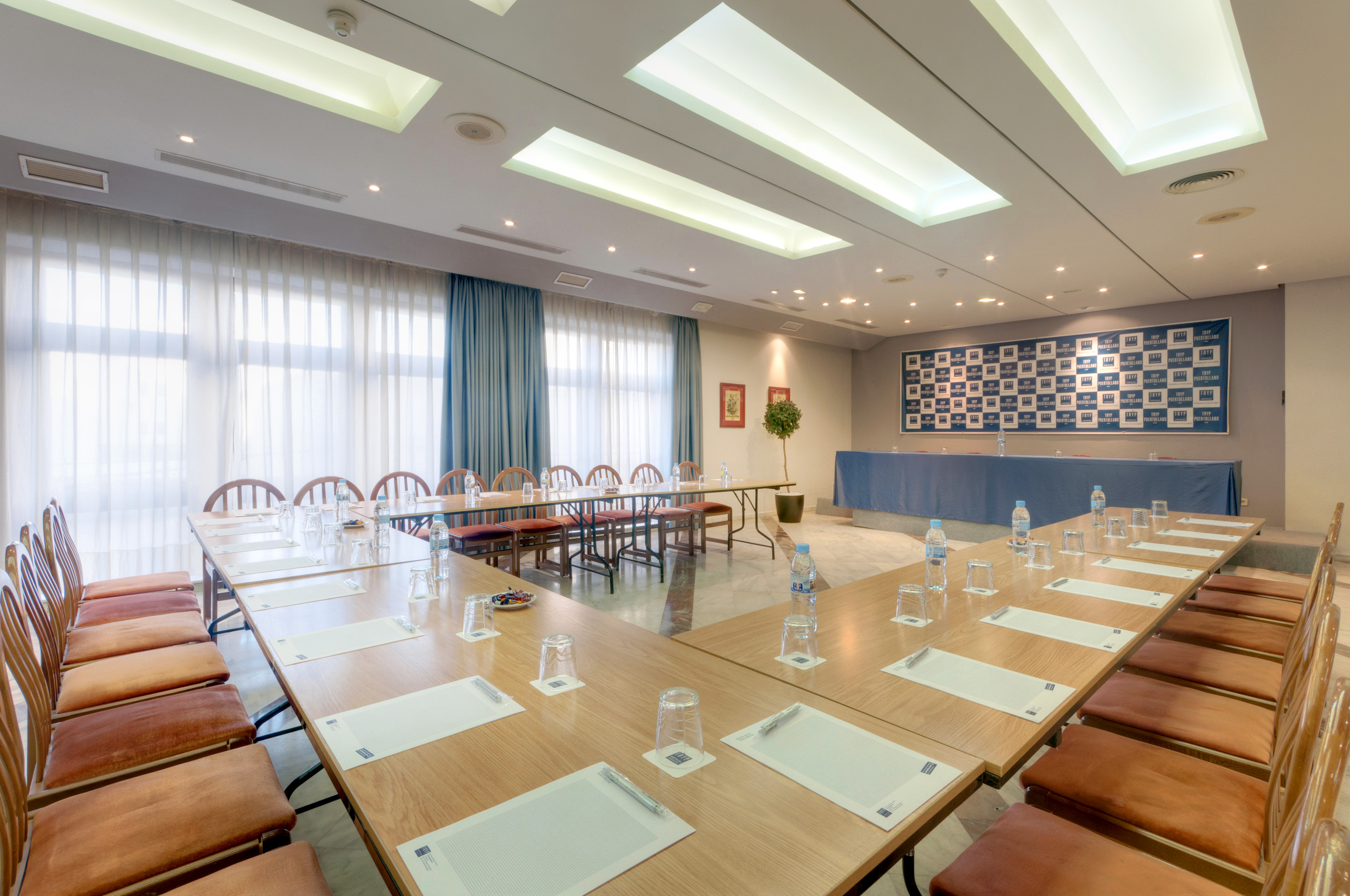 U-shaped meeting room setup with tables, chairs, water, and notepads.