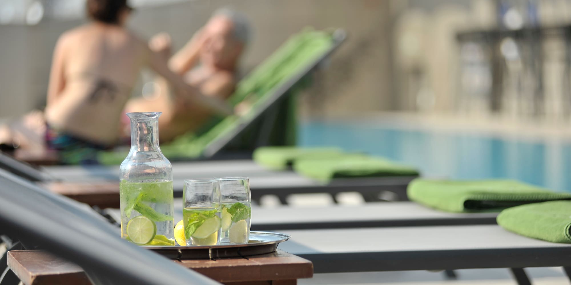 a glass bottle and glasses with lemons on a table with chairs and a man in the background