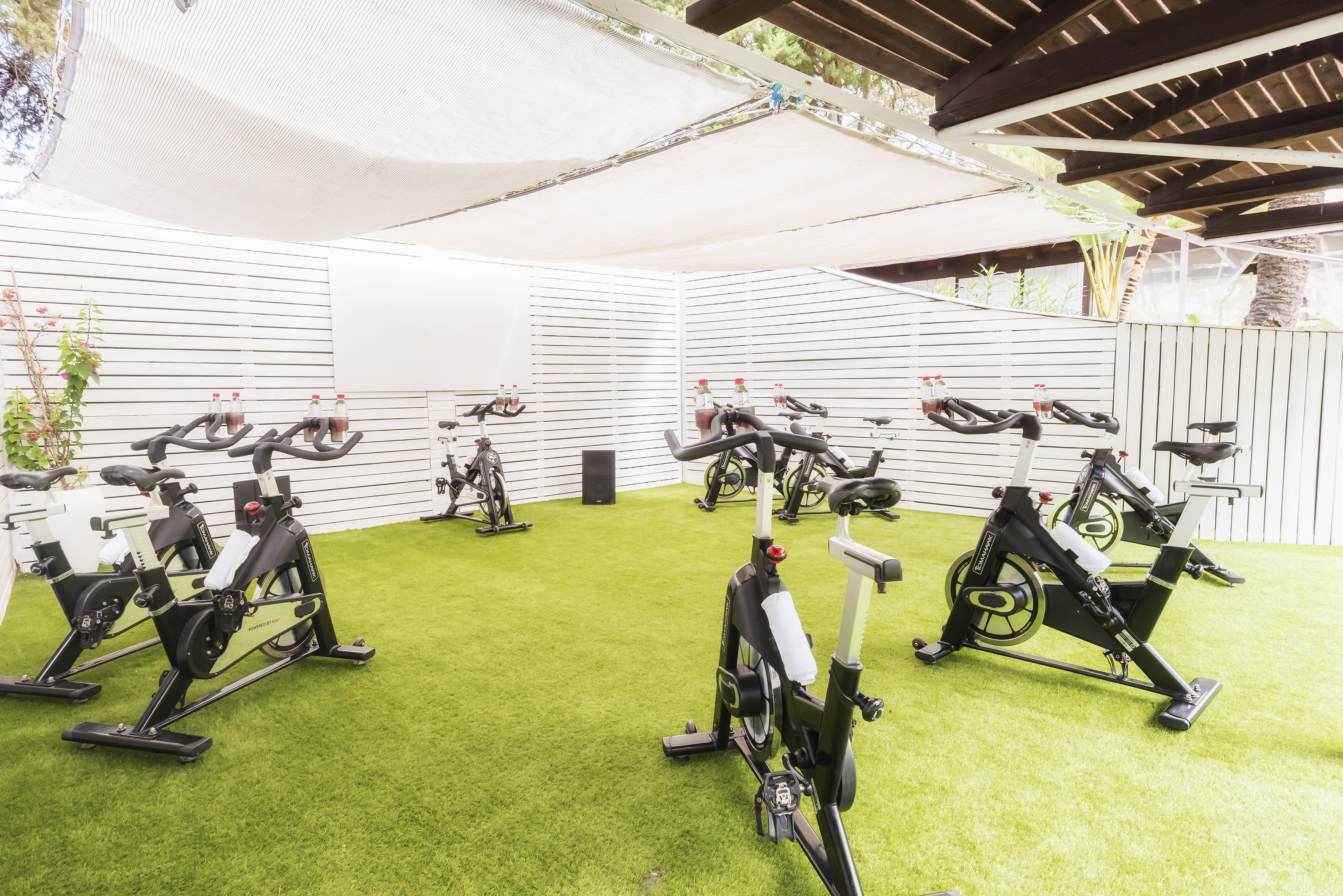 Spinning bikes on green turf in a covered outdoor gym area.