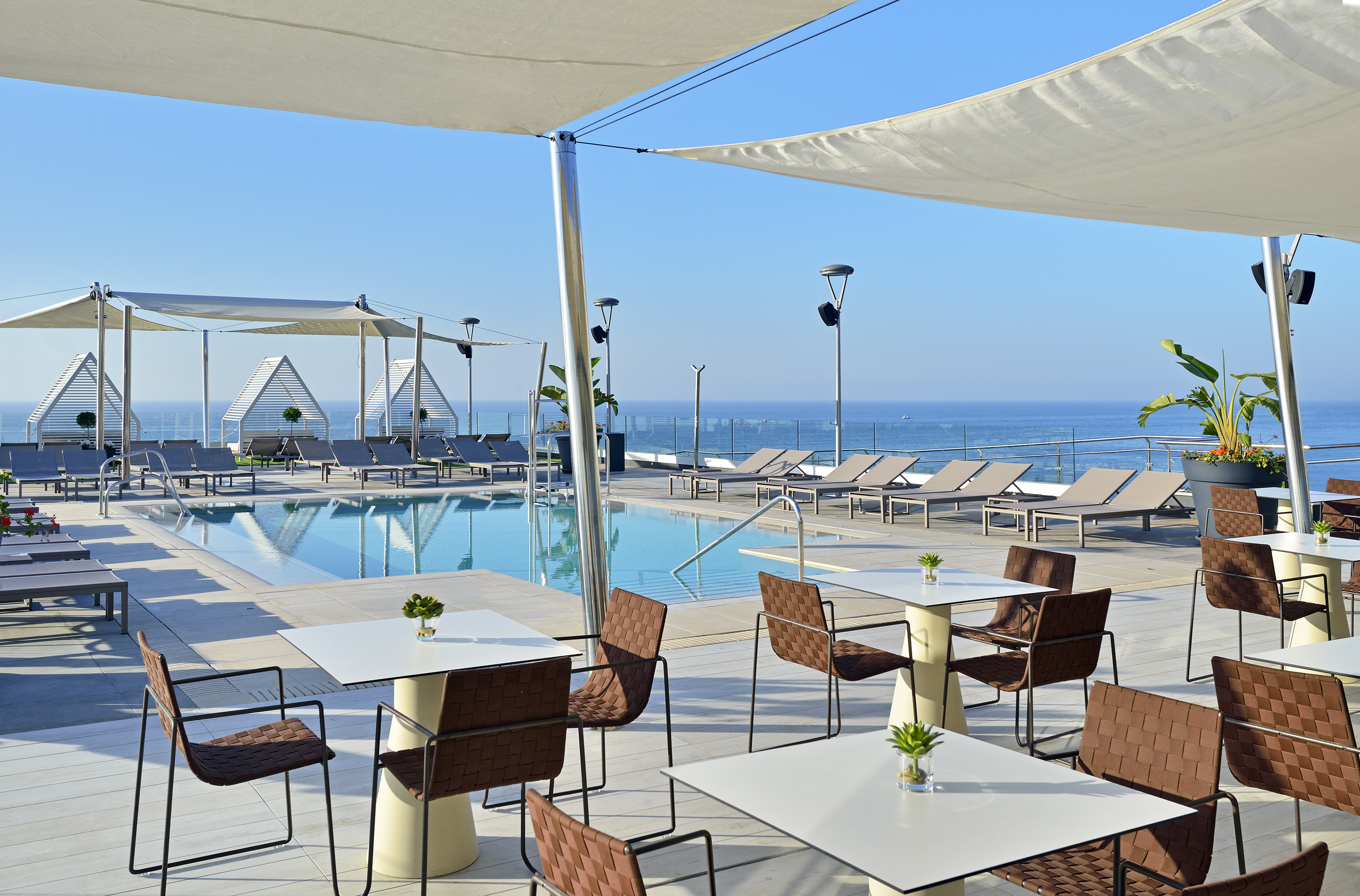 Modern rooftop pool deck with ocean views, lounge chairs, and outdoor dining.