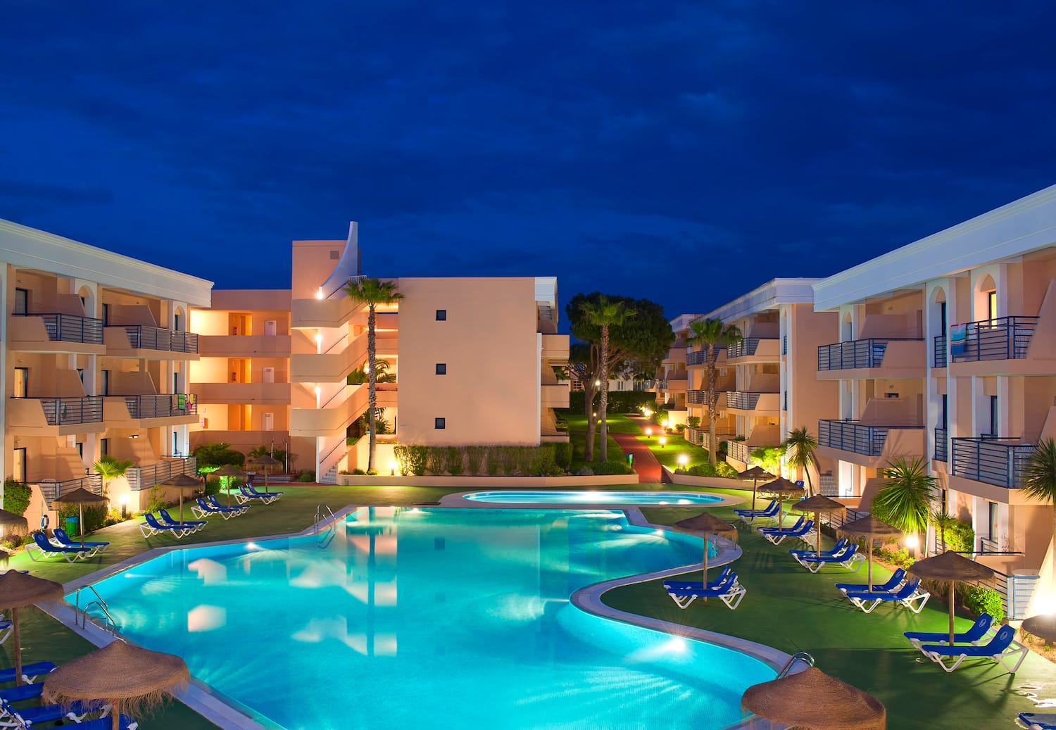 a pool with lounge chairs and a building with a dark sky
