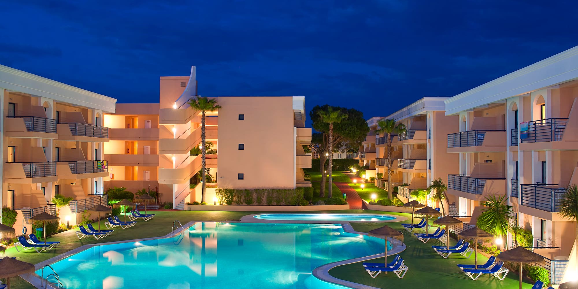 a pool with lounge chairs and a building with a dark sky